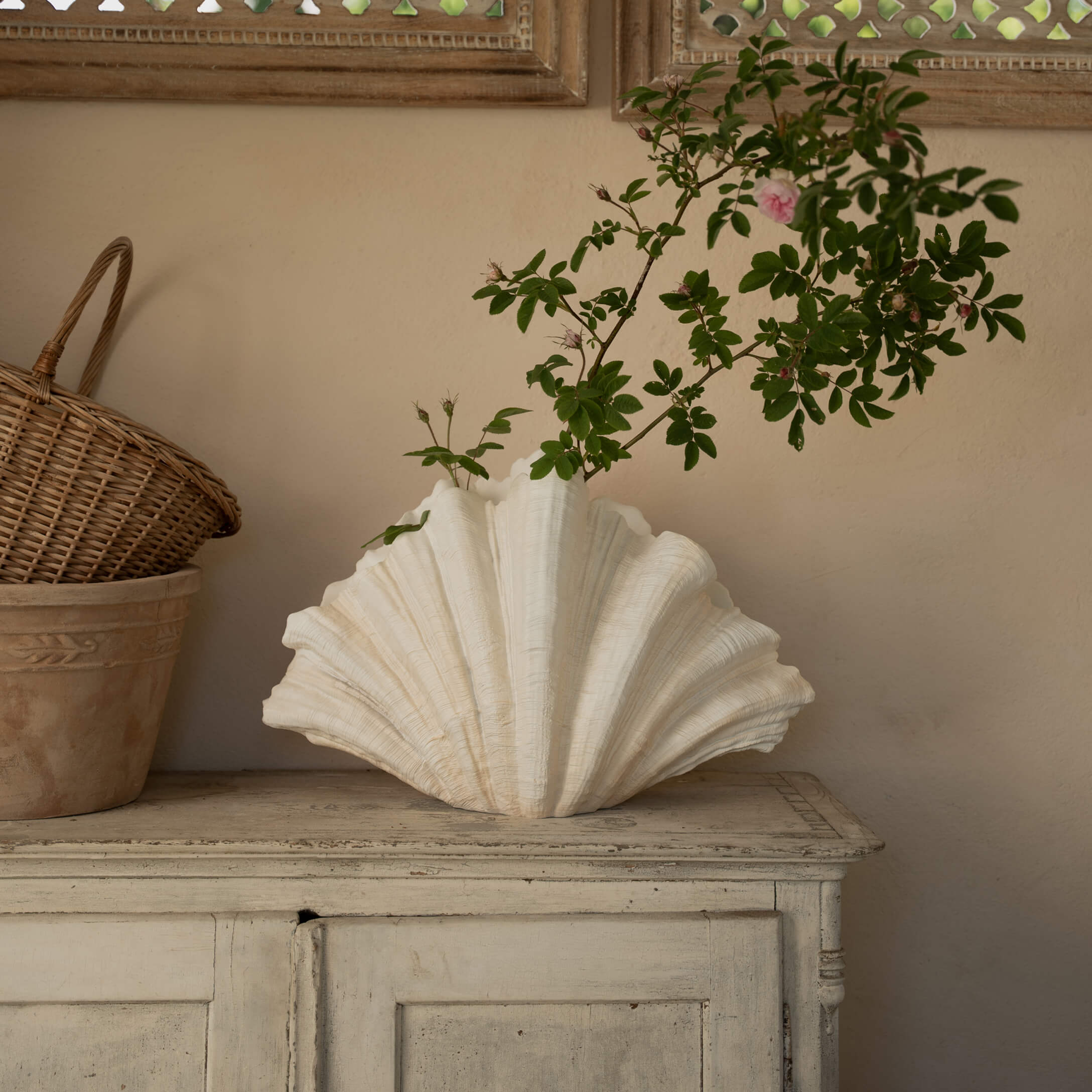 Vase en céramique blanche en forme de coquillage avec des branches vertes sur une commode en bois
