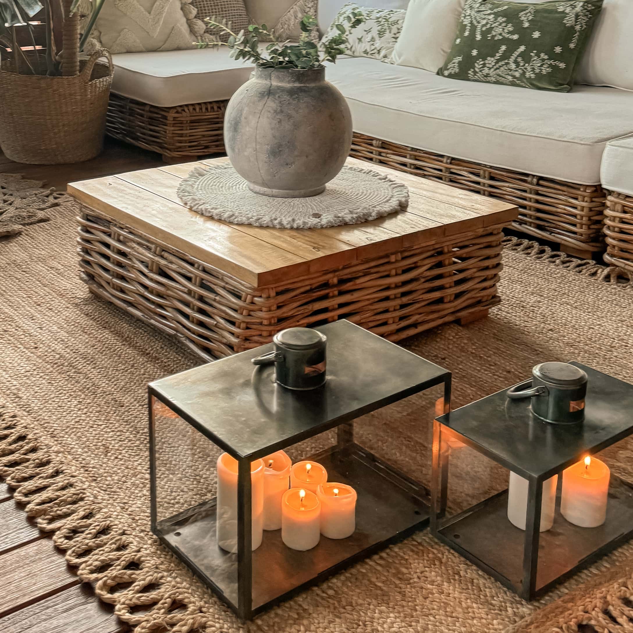 Lanterne en métal avec bougies allumées sur tapis près d'une table basse en osier et canapé beige