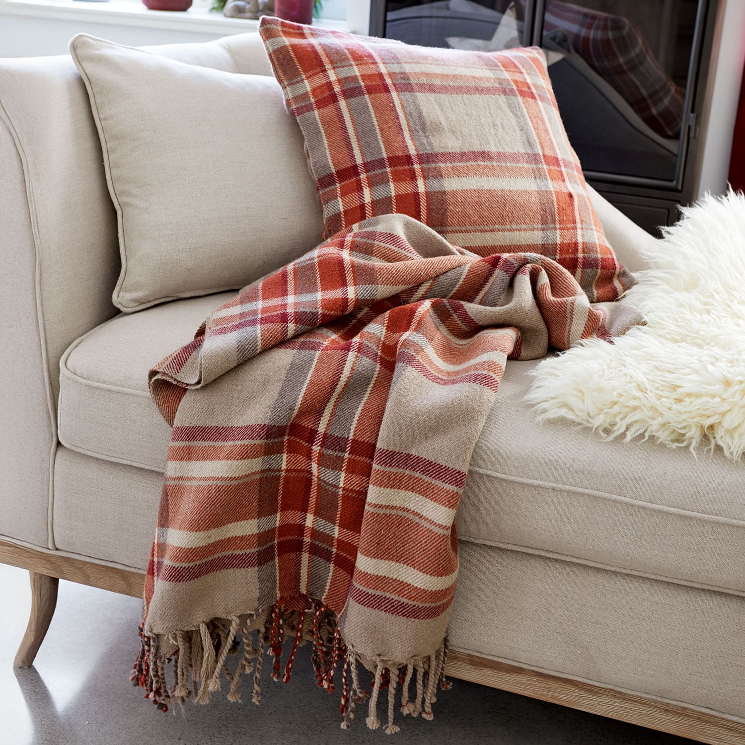 Canapé beige avec coussin et plaid à carreaux rouges et bruns pour un salon chaleureux