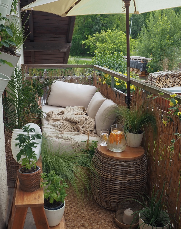 Balcon cosy avec canapé beige, coussins, table en osier, plantes et parasol pour détente extérieure
