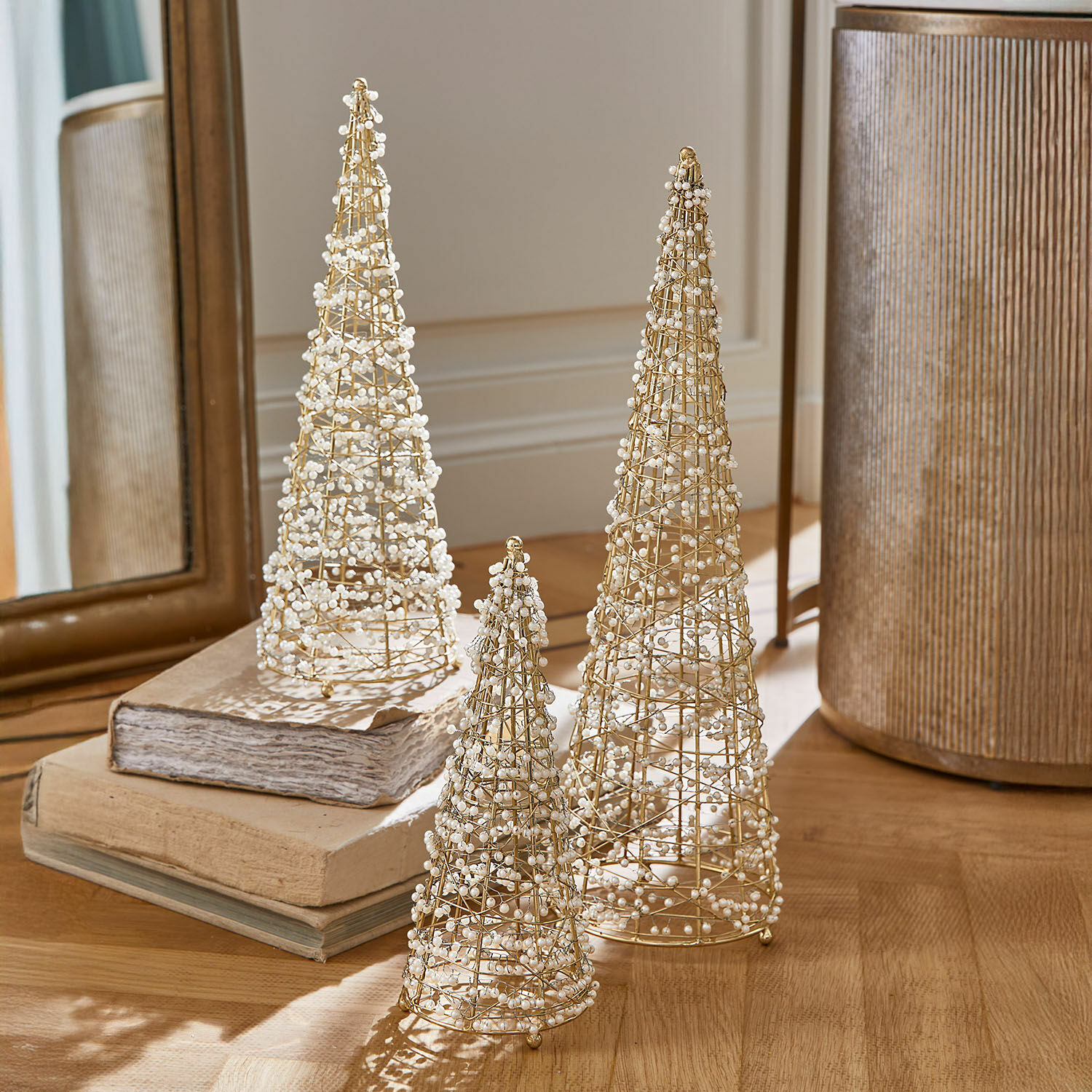 Lot de 3 sapins décoratifs Amelioro Ensemble de trois cônes décoratifs en fil doré ornés de perles blanches sur une table en bois