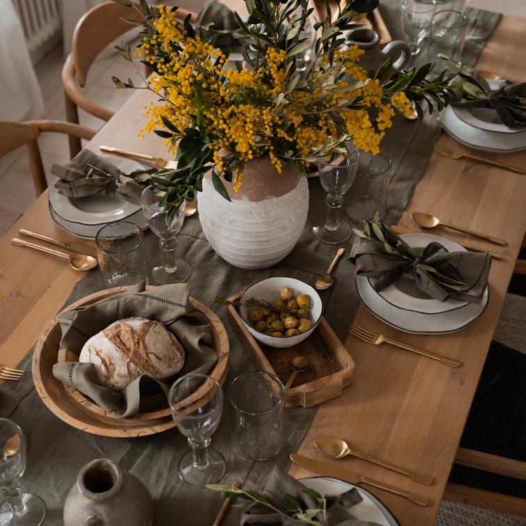Table rustique en bois avec vaisselle blanche, bols en bois et fleurs jaunes en vase en argile