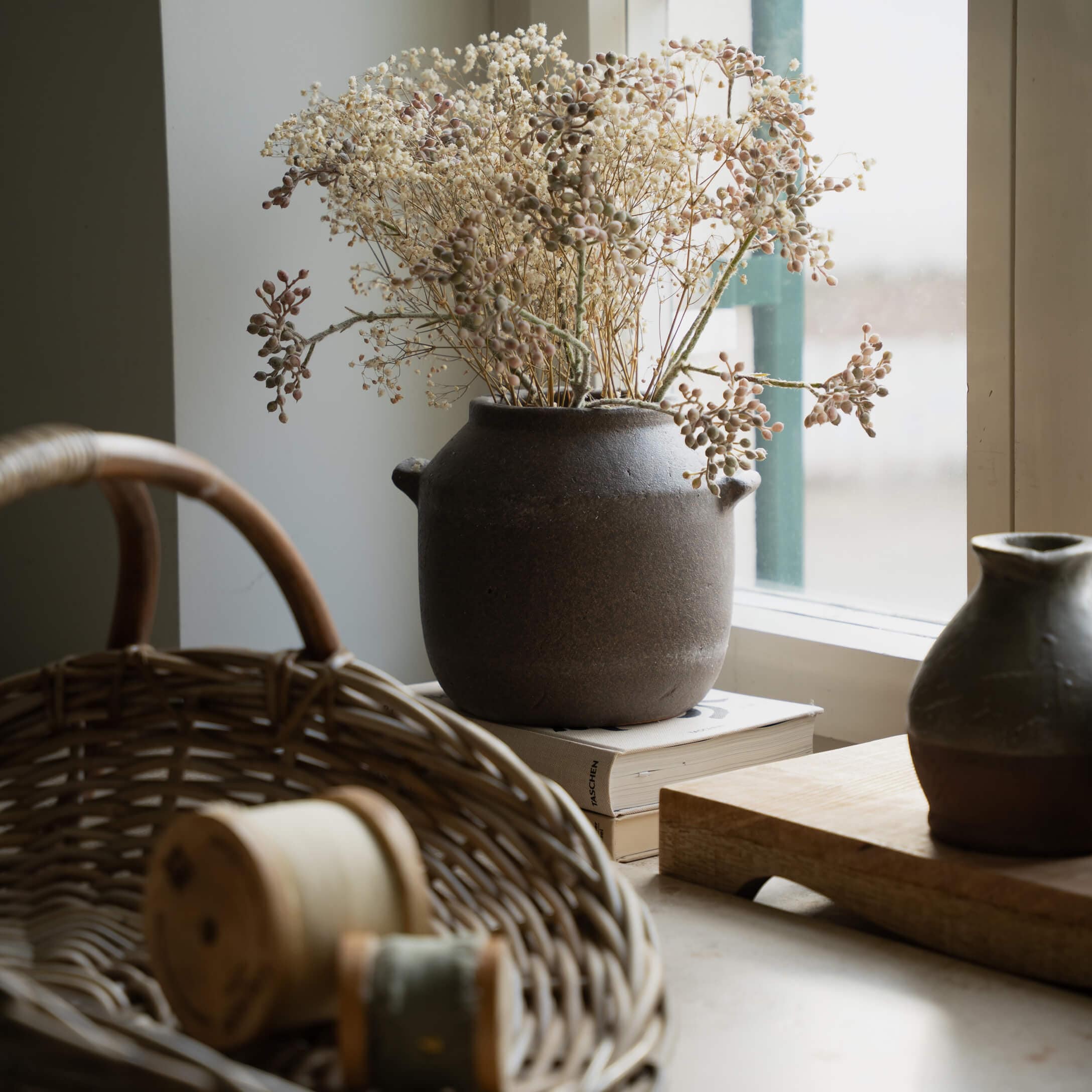 Vase en céramique marron avec fleurs séchées sur le rebord de la fenêtre près d'un panier en osier