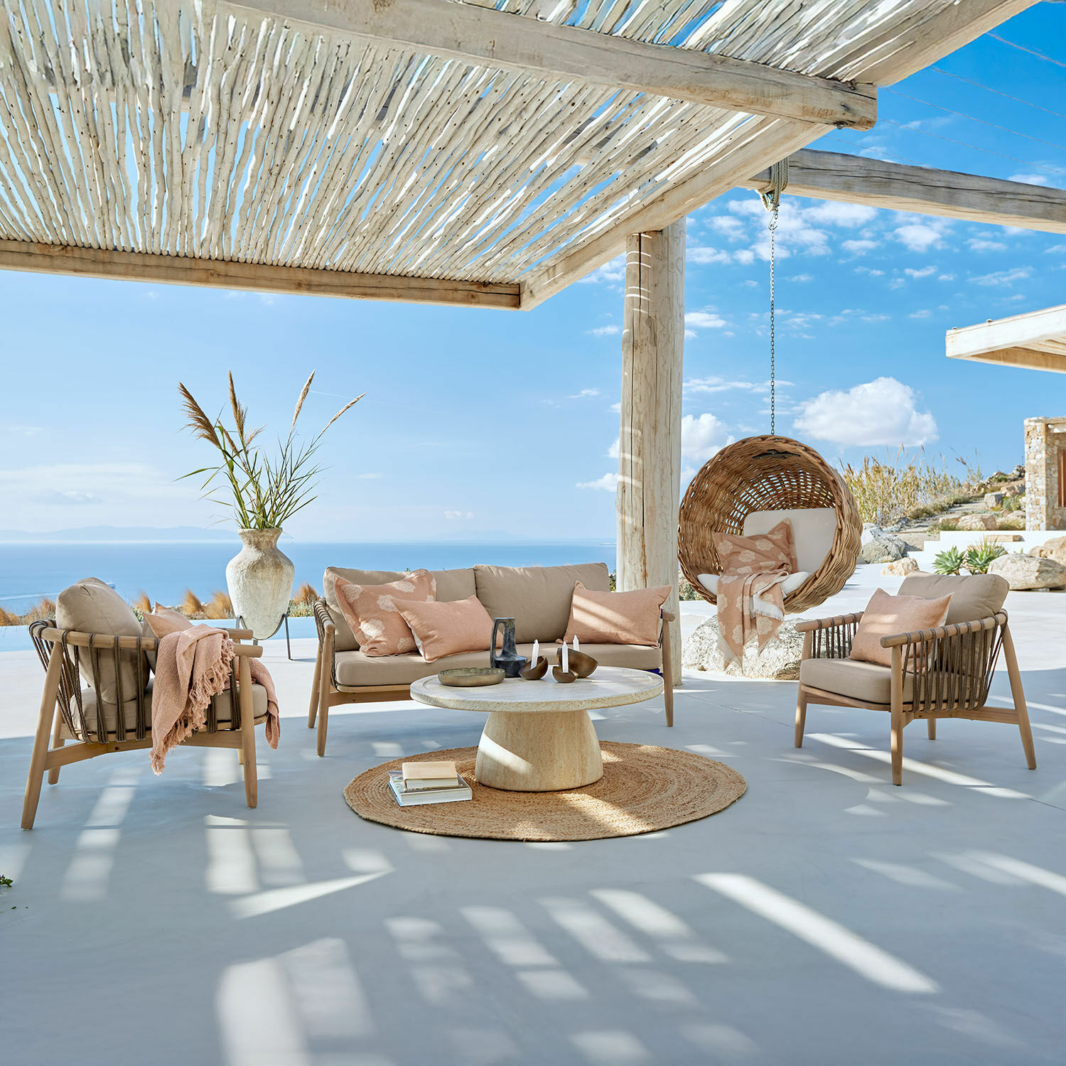 Salon de jardin FSC®-100% Thornwick Ensemble de mobilier d'extérieur beige avec coussins et fauteuil suspendu en osier sur terrasse face à la mer