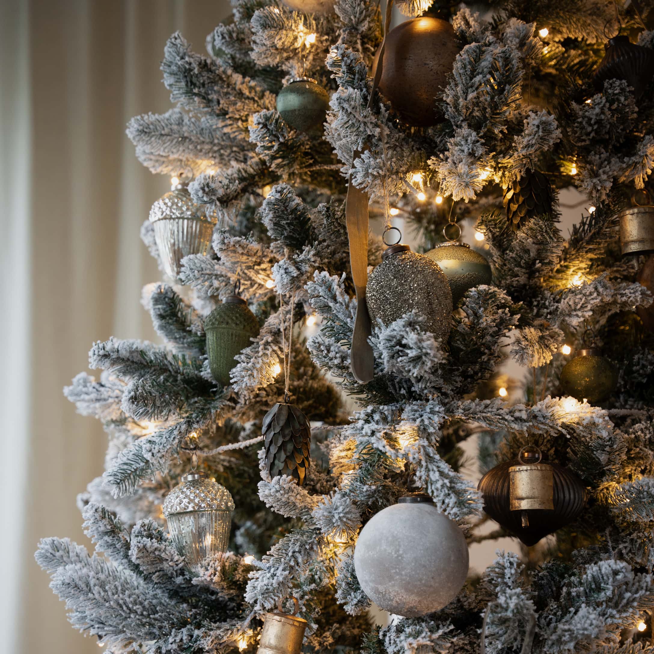 Détail d'un sapin de Noël artificiel enneigé avec décorations dorées et vertes et lumières LED