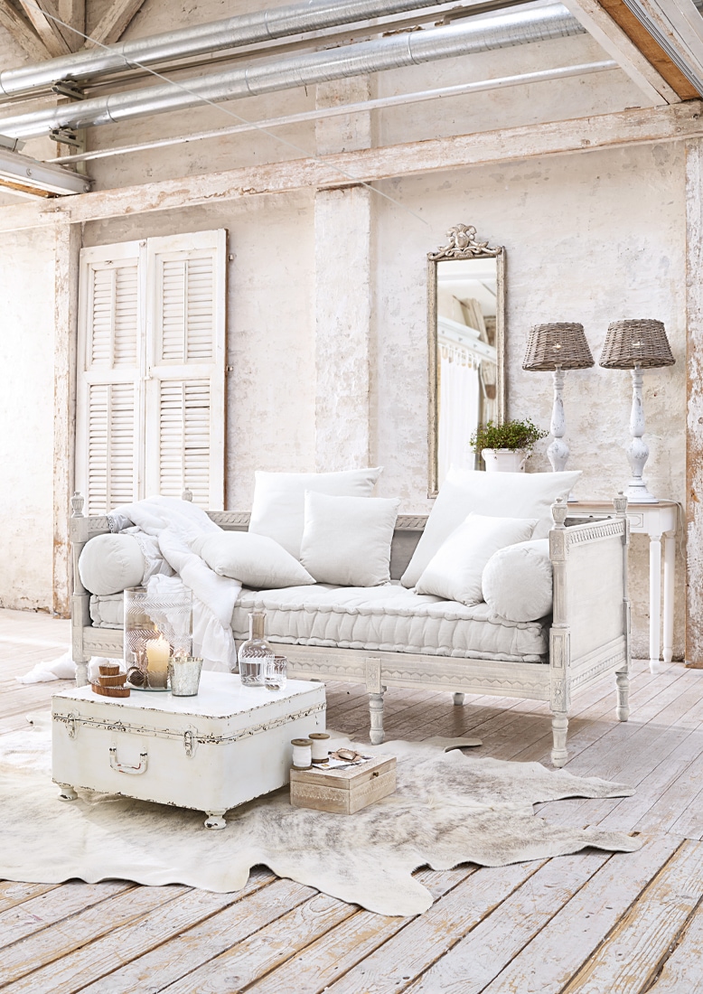 Canapé en bois blanc avec coussins clairs et miroir décoratif dans un intérieur rustique lumineux