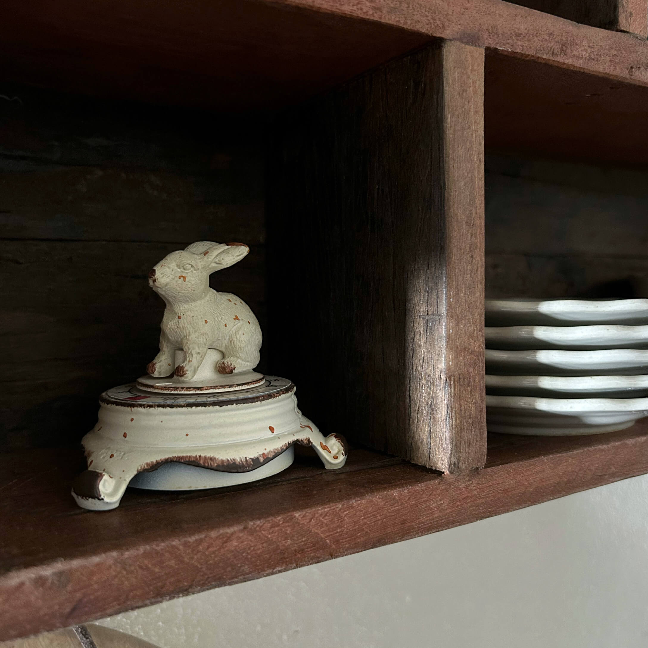 Boîte en céramique blanche avec couvercle lapin sur étagère en bois à côté d'assiettes
