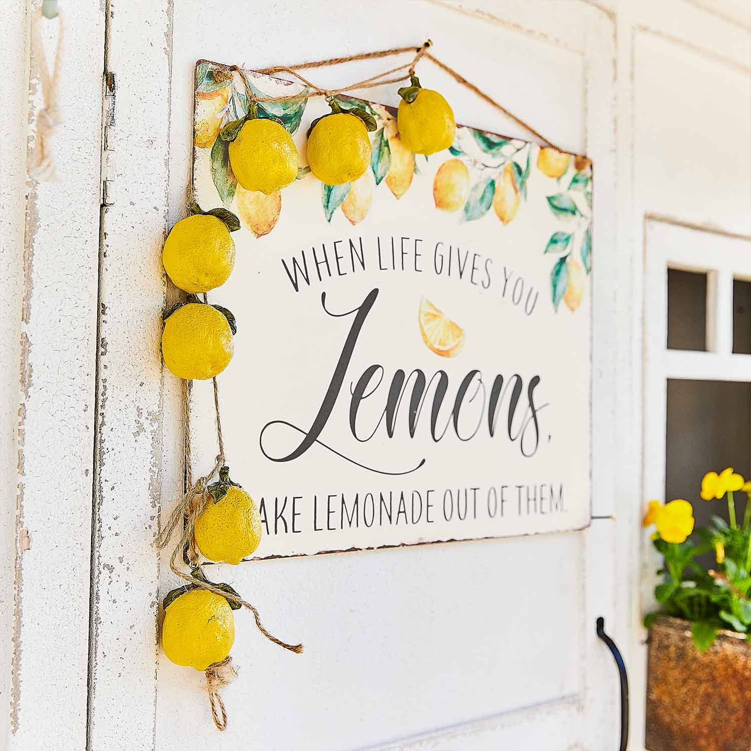 Panneau décoratif avec motif citron et guirlande de citrons jaunes suspendue sur une porte blanche