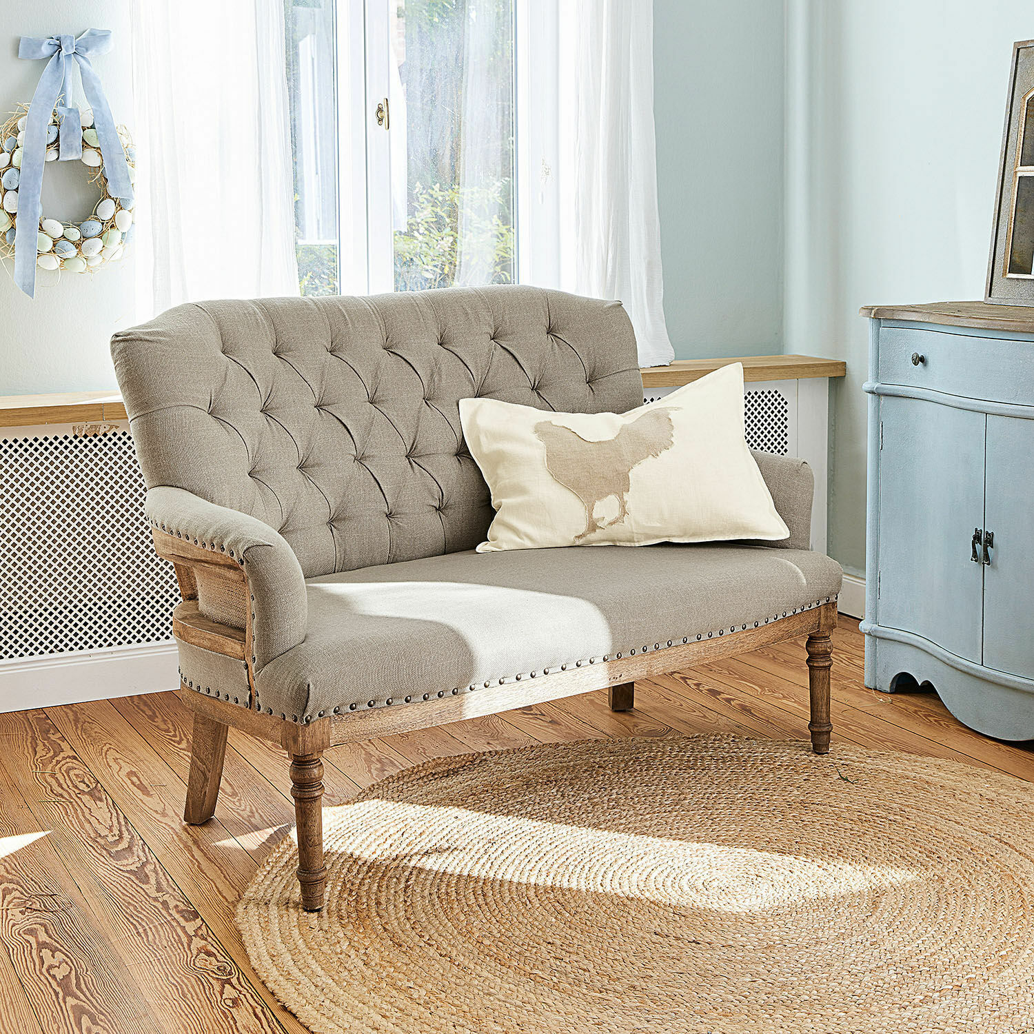 Canapé Kingsley Canapé beige capitonné avec cadre en bois et coussin décoratif dans un salon lumineux