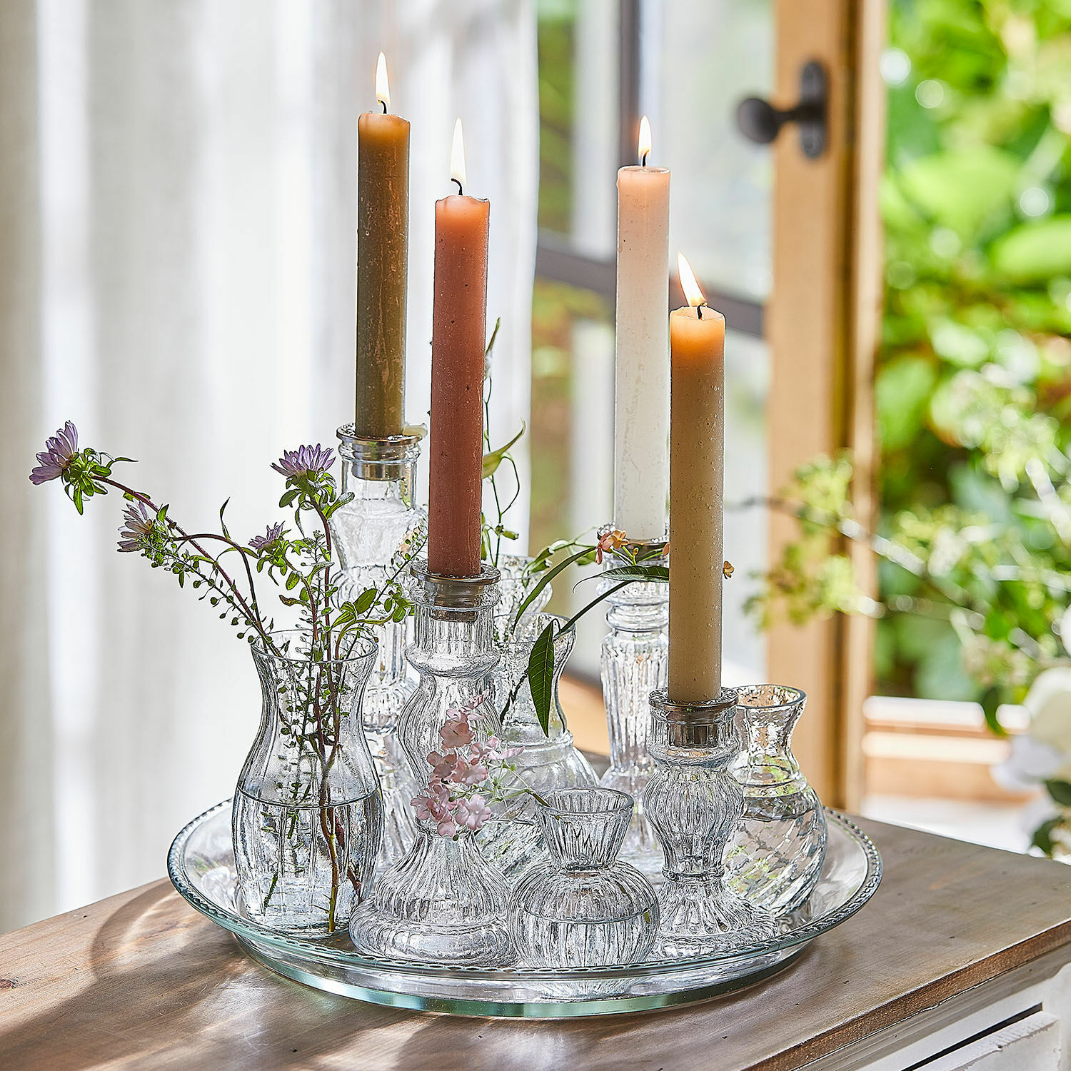 Lot de 12 bougies Bauceau Bougeoirs et petits vases en verre avec bougies colorées et fleurs sur un plateau en verre sur une table en bois