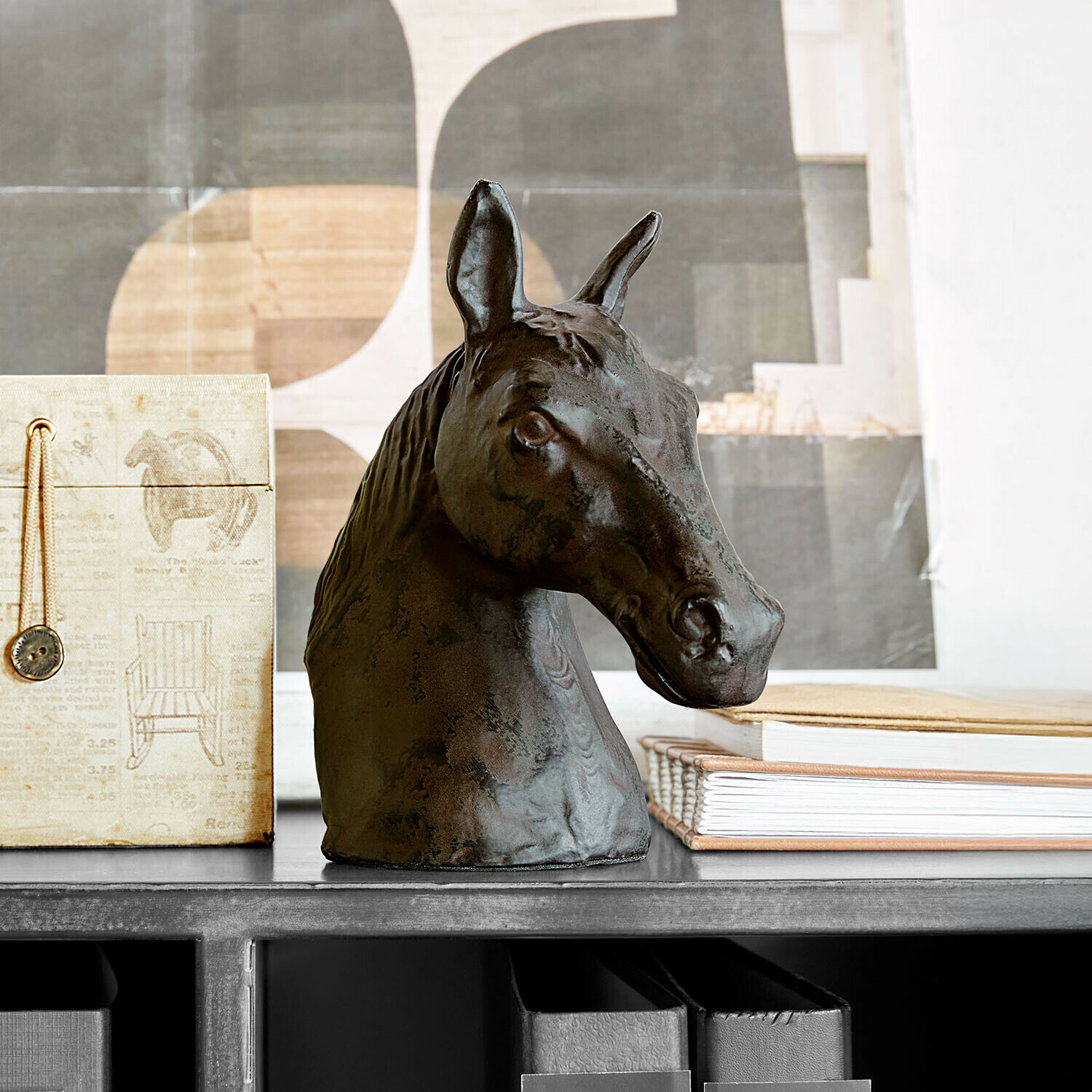 Tête de cheval décorative en métal foncé posée sur une étagère avec livres et boîte
