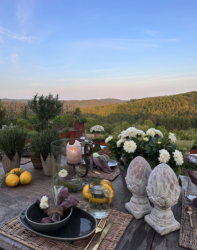 Table rustique avec décorations en pierre et fleurs blanches sur fond de collines verdoyantes et ciel bleu