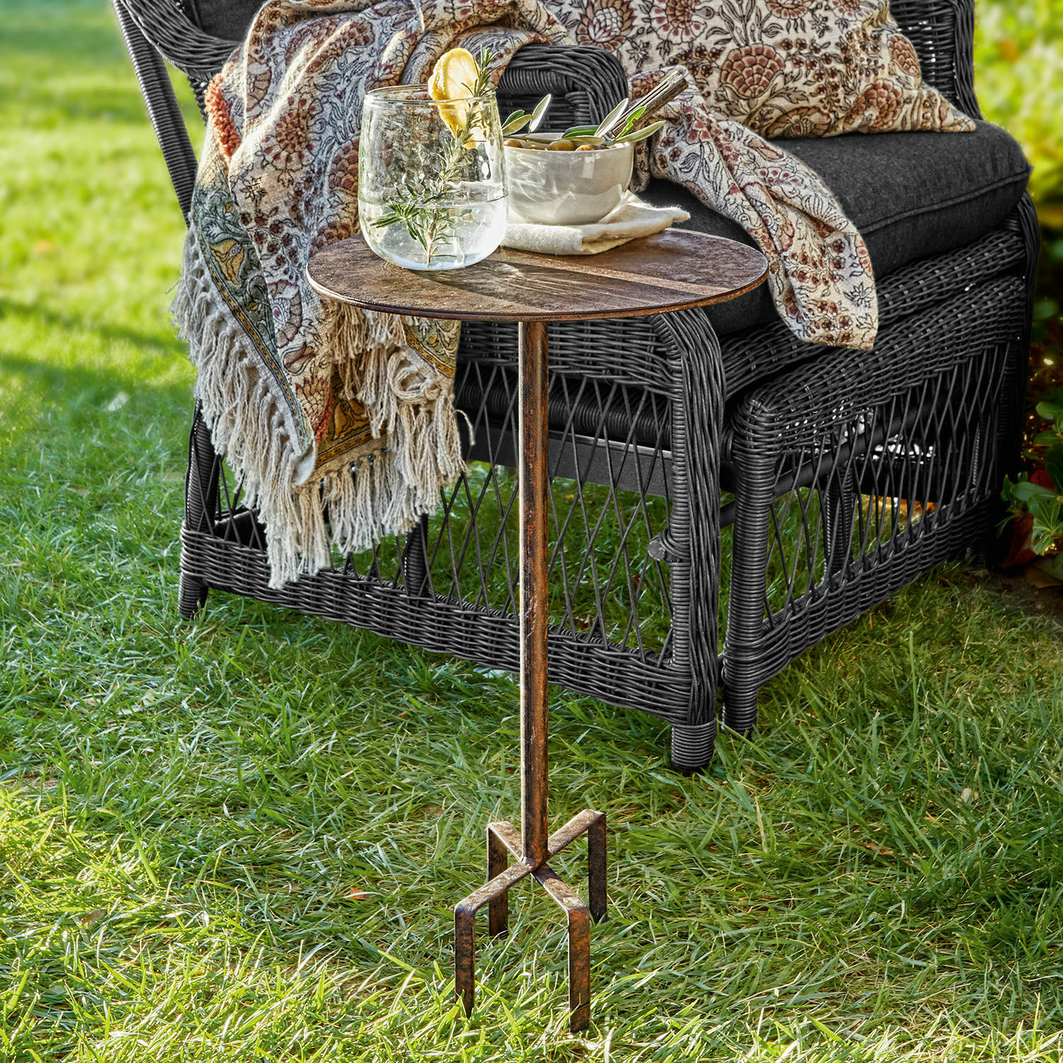 Petite table Fermont Table d'appoint en métal patiné style vintage sur l'herbe près d'un fauteuil en osier avec coussin et plaid