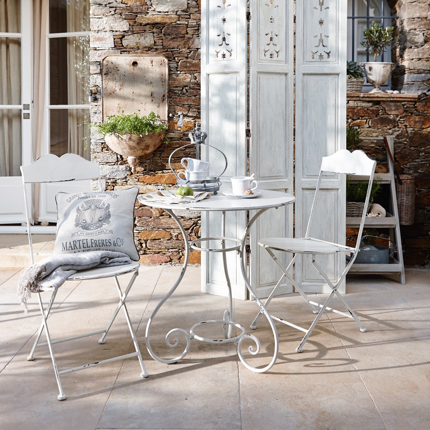 Ensemble table et chaises Iteuil Table ronde et deux chaises pliantes blanches en métal style vintage sur terrasse en pierre décorée