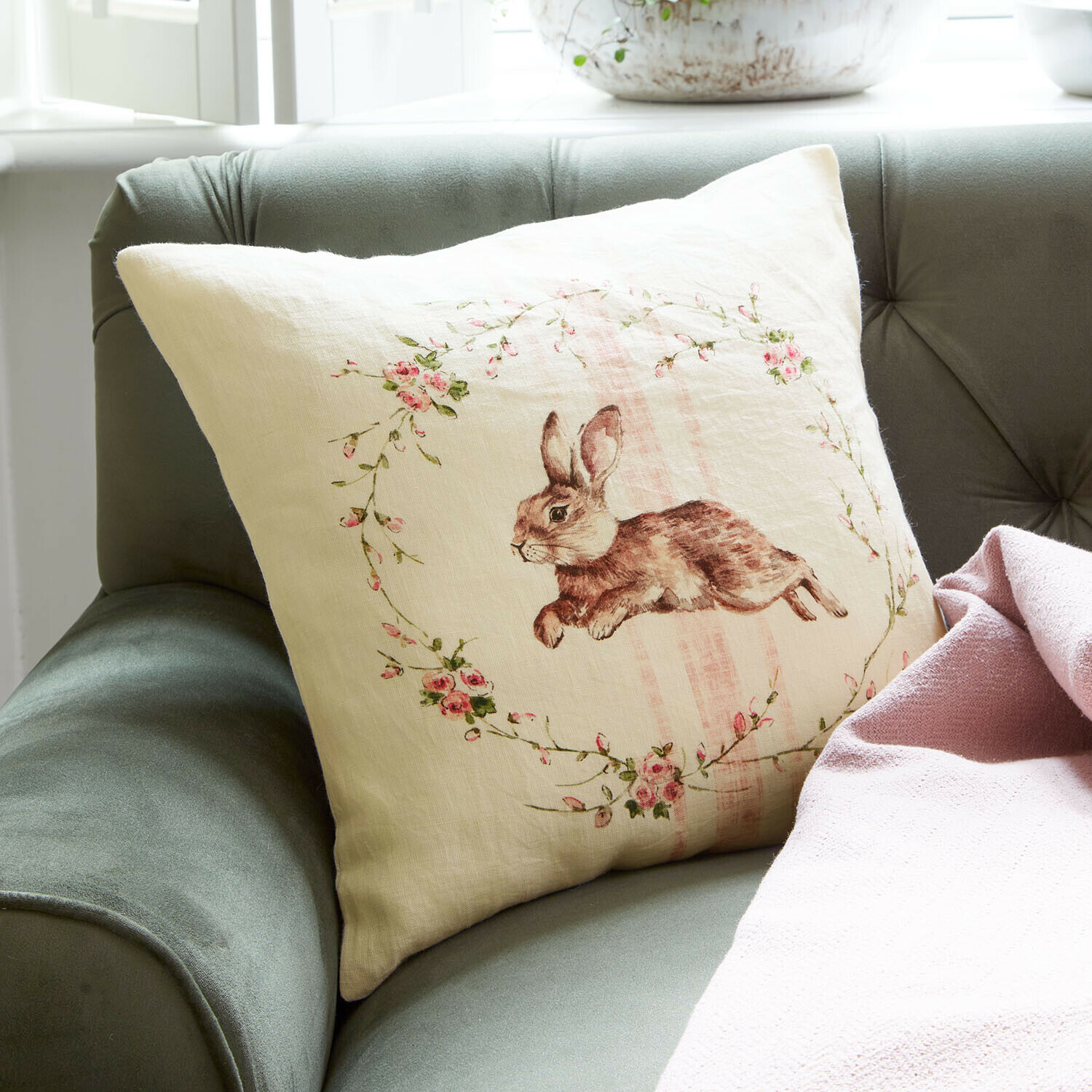 Housse de coussin Ravencrest Coussin en lin beige avec imprimé lapin et fleurs roses sur canapé vert avec couverture rose