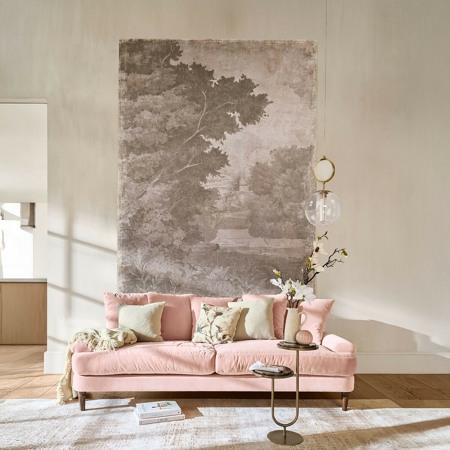 Papier peint panoramique Jarville Canapé en velours rose avec coussins et table d'appoint fleurie dans un salon lumineux avec décoration murale