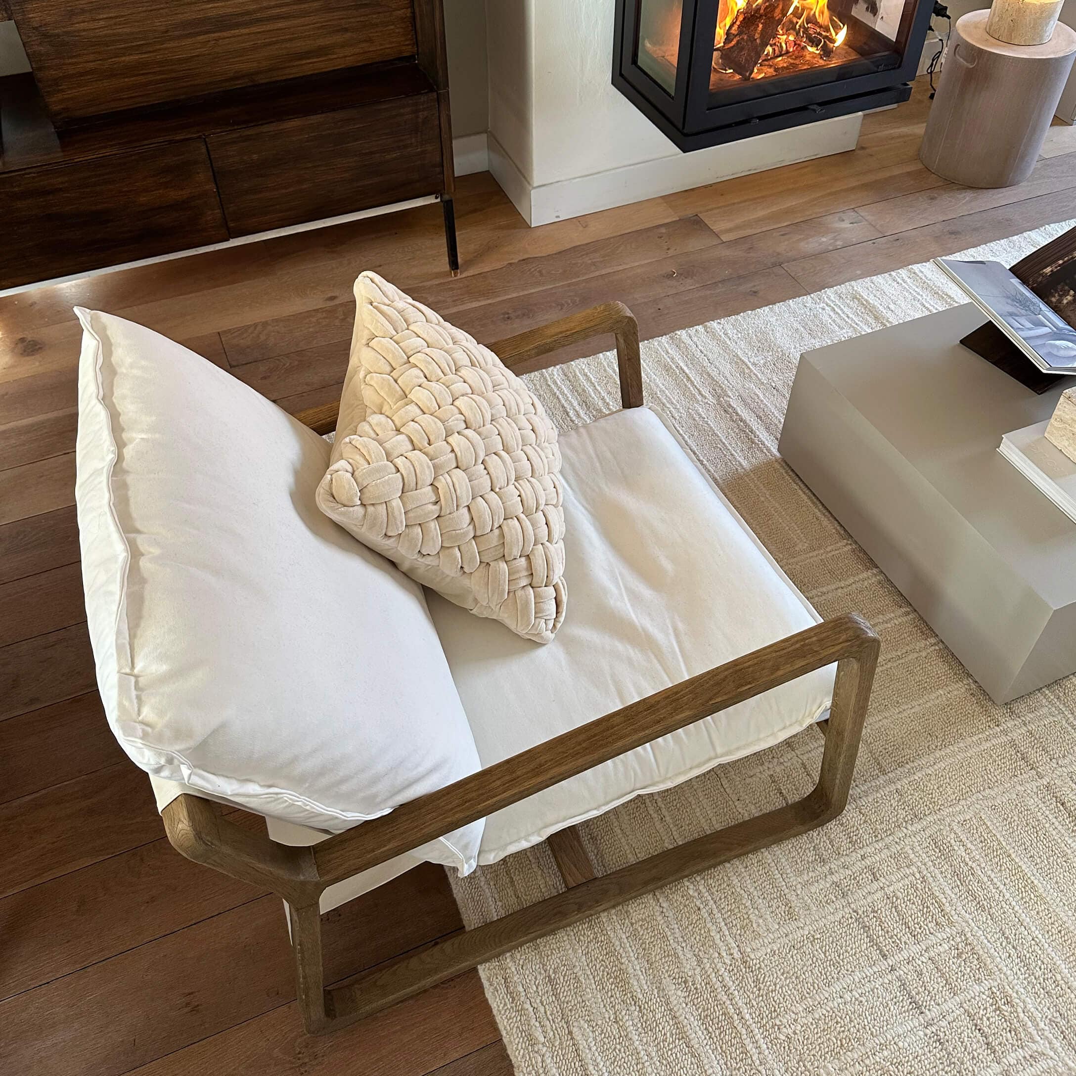 Fauteuil en bois avec coussins crème sur tapis clair près d'une cheminée dans un salon moderne
