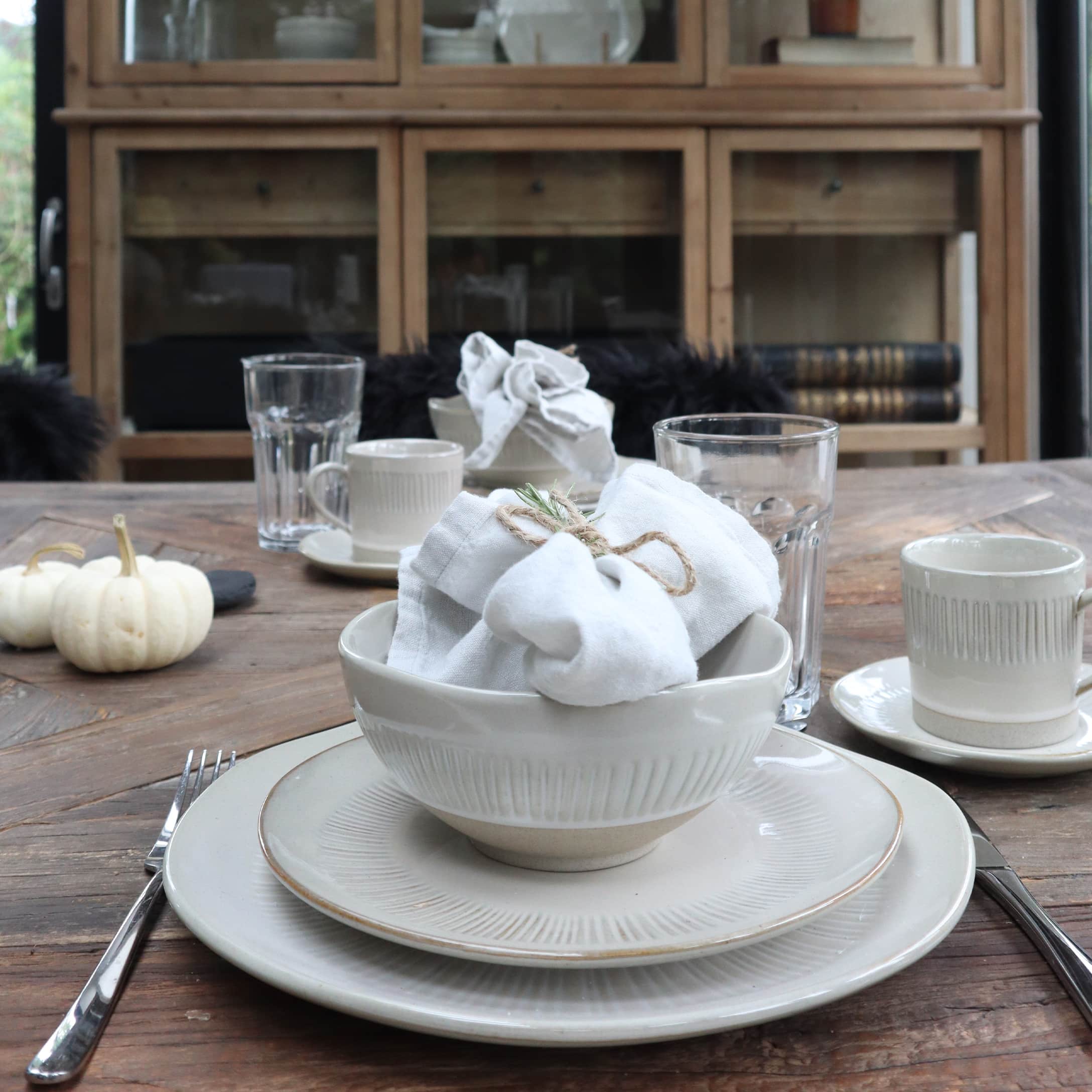 Service de vaisselle en céramique blanche sur table en bois avec décorations de citrouilles et verres à eau