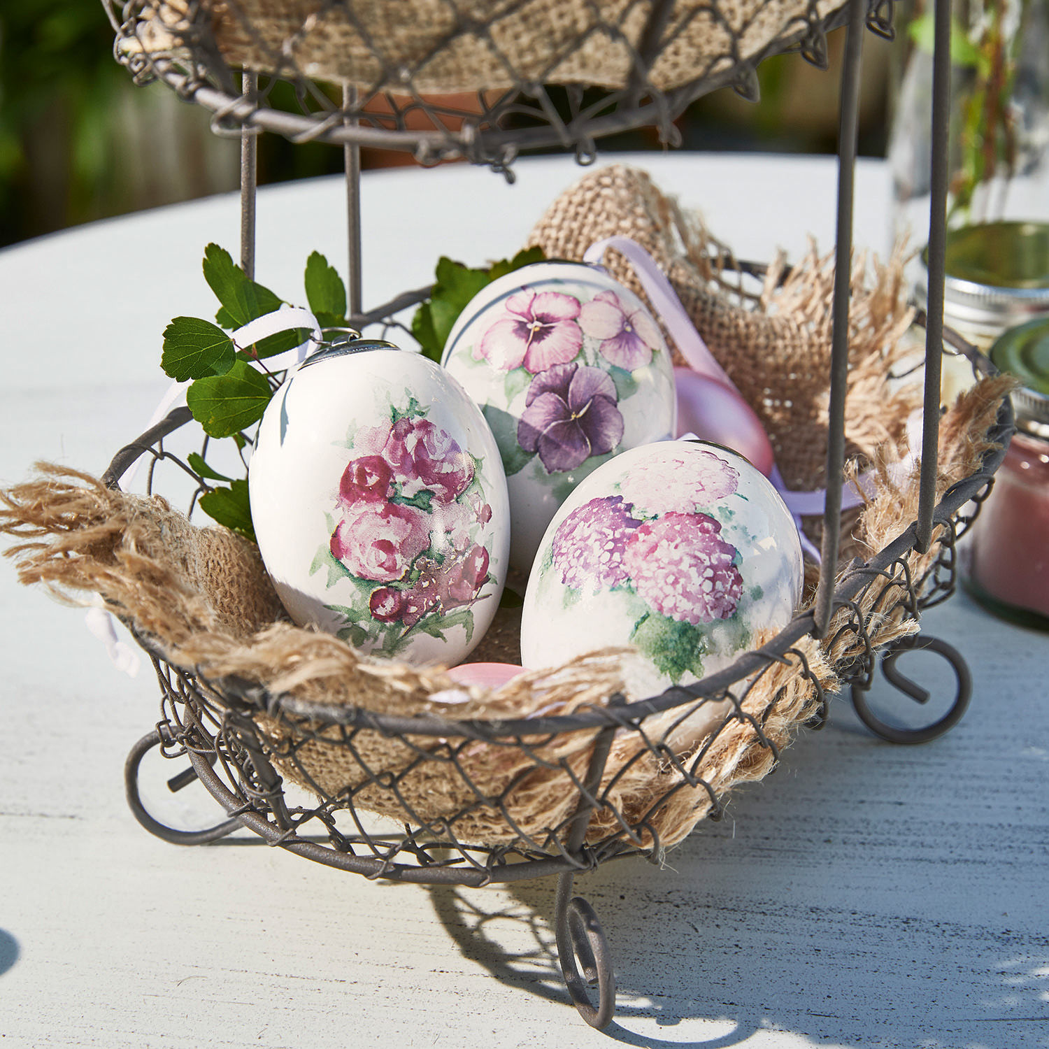 Lot de 3 œufs de Pâques Maurine Œufs décoratifs blancs avec motifs floraux dans un panier en métal sur une table extérieure