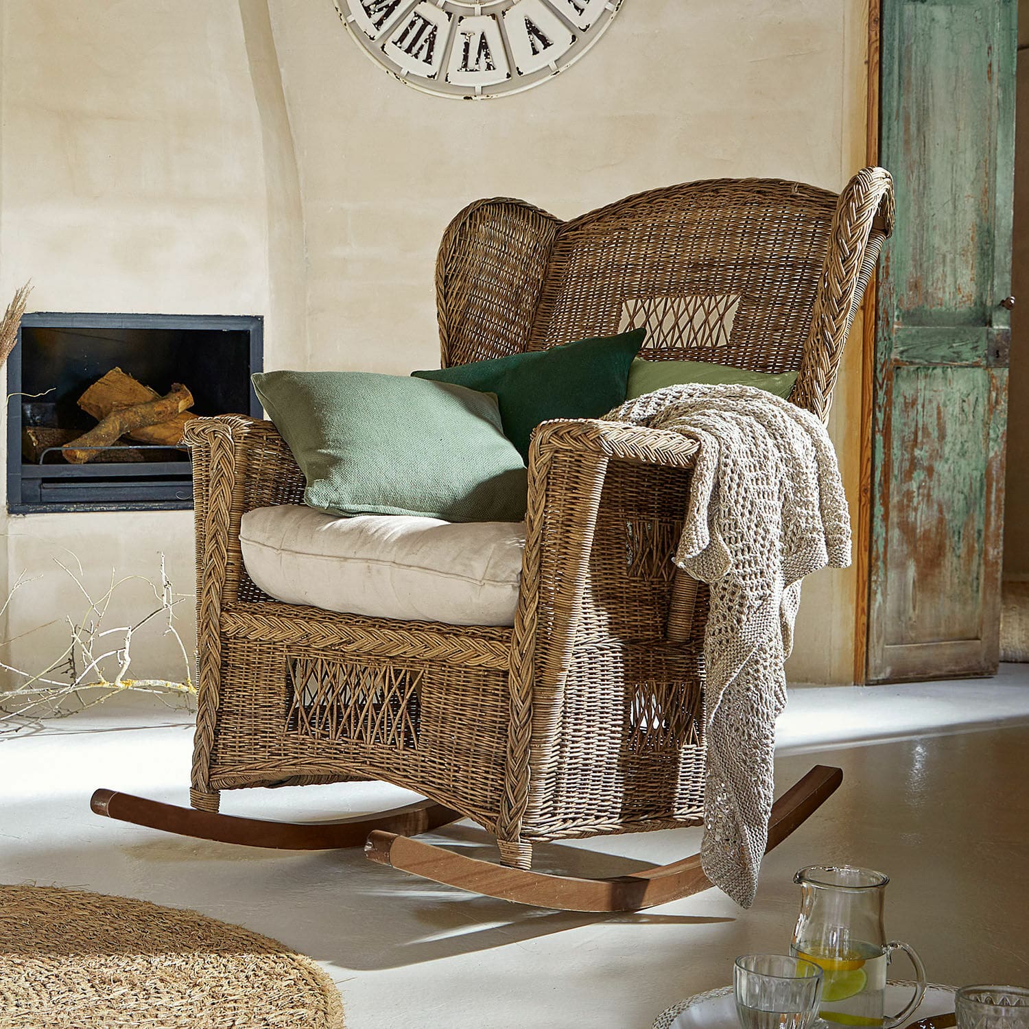 Fauteuil à bascule Jeveren Fauteuil à bascule en rotin naturel avec coussins verts et plaid dans un intérieur chaleureux