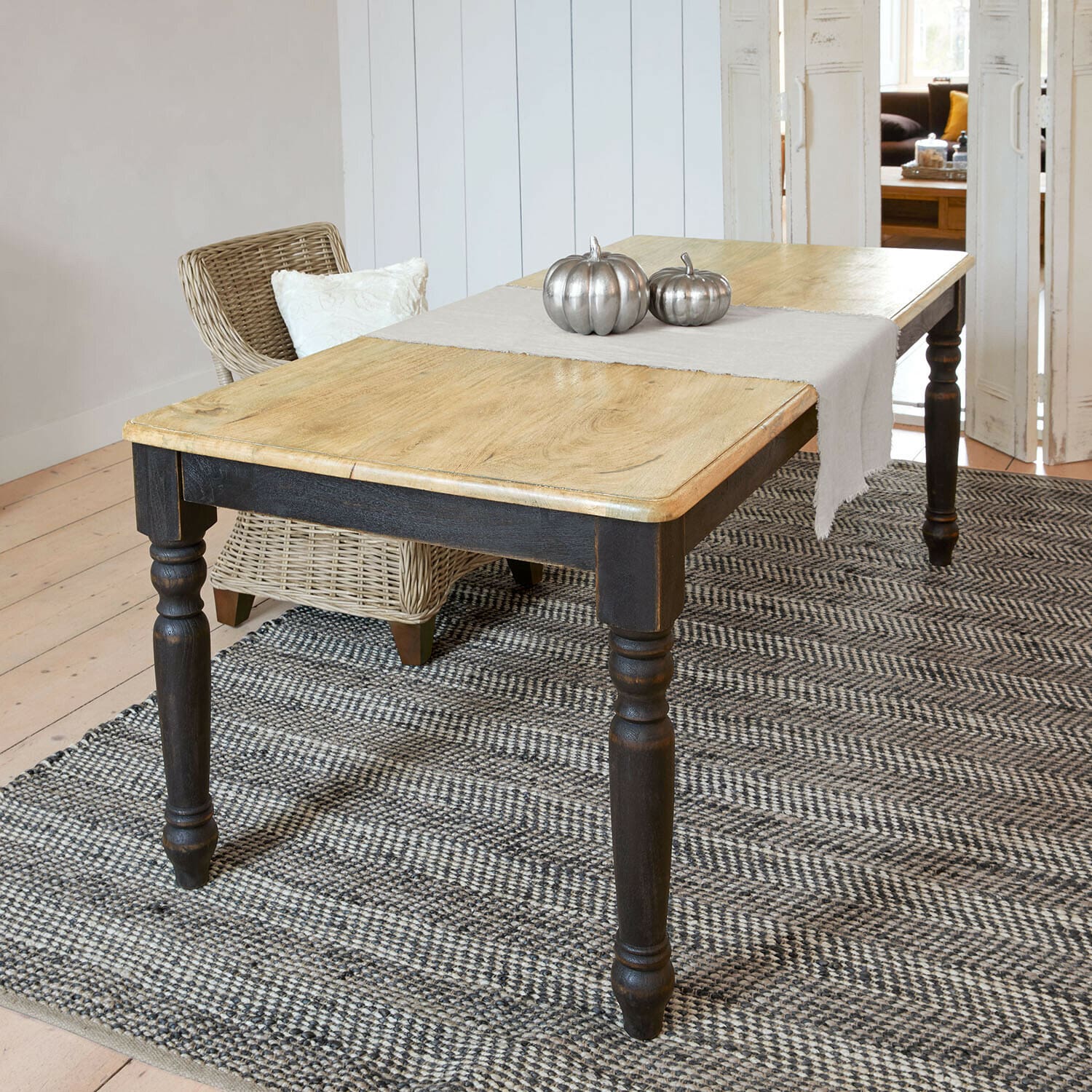 Table Mont Lisan Table en bois clair avec pieds noirs sur tapis gris, décorée de citrouilles métalliques argentées