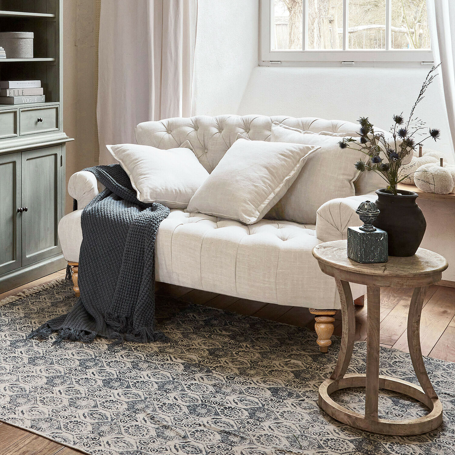 Canapé Springfield Village Canapé capitonné beige en lin avec coussins et plaid gris tricoté dans un salon chaleureux avec table en bois