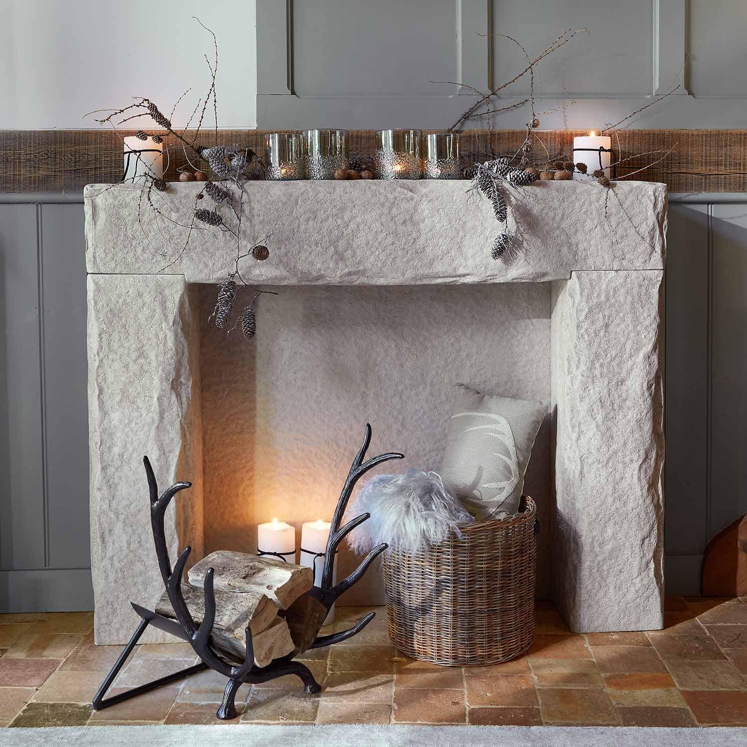 Cheminée en pierre blanche avec décorations de branches et bougies, panier en osier avec coussin et plaid en fourrure