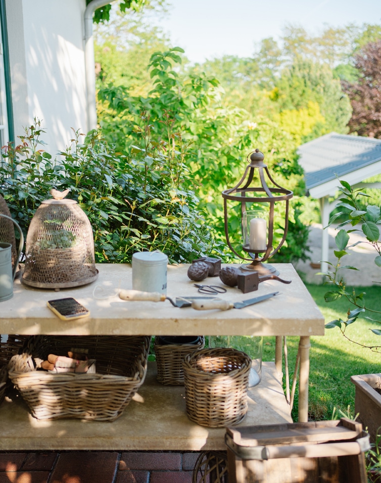 Table de jardin en pierre avec paniers en osier, outils de jardinage et lanterne à bougie