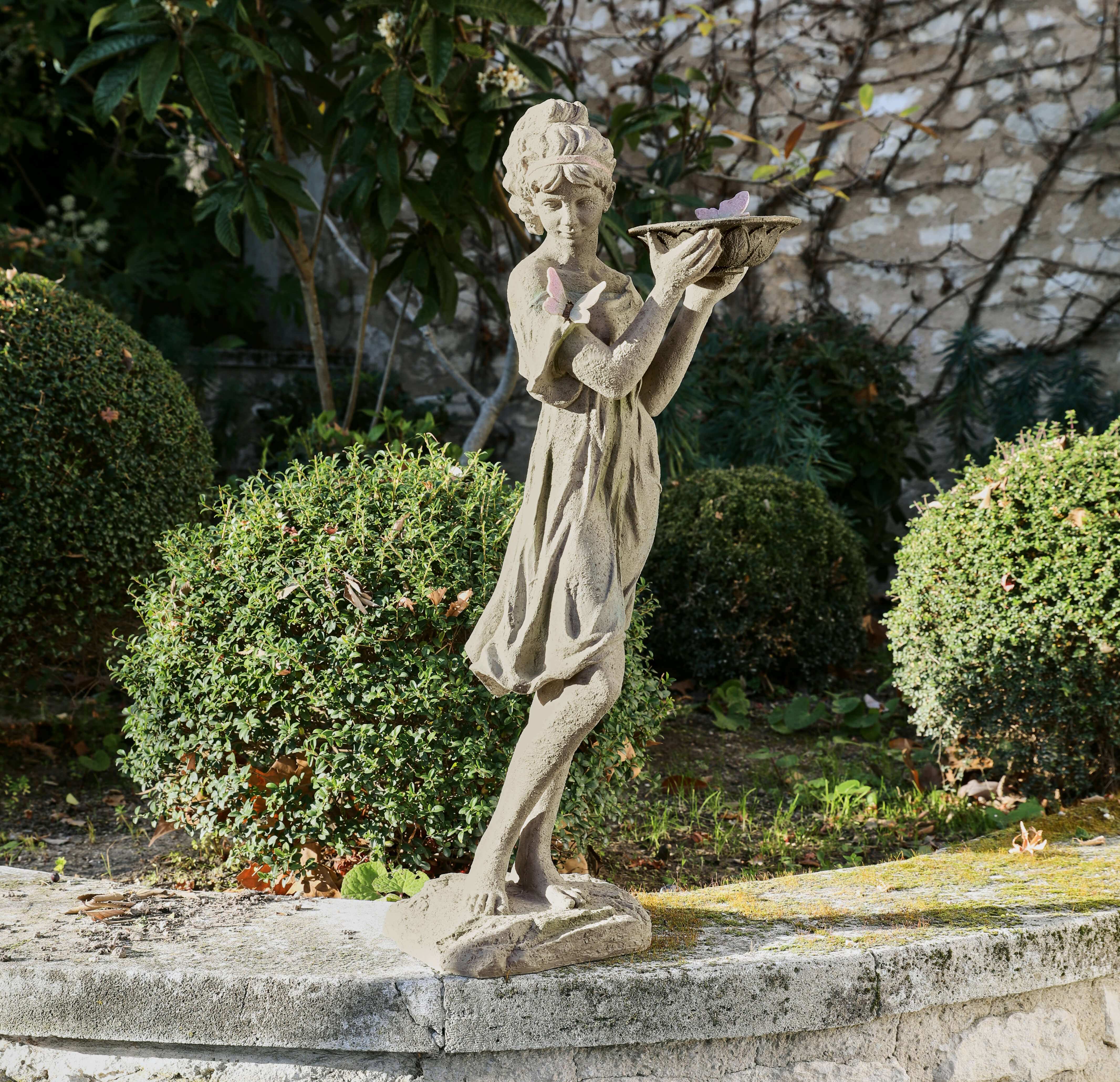 Statue de jardin en béton représentant une fillette avec des papillons, décoration extérieure dans un jardin vert