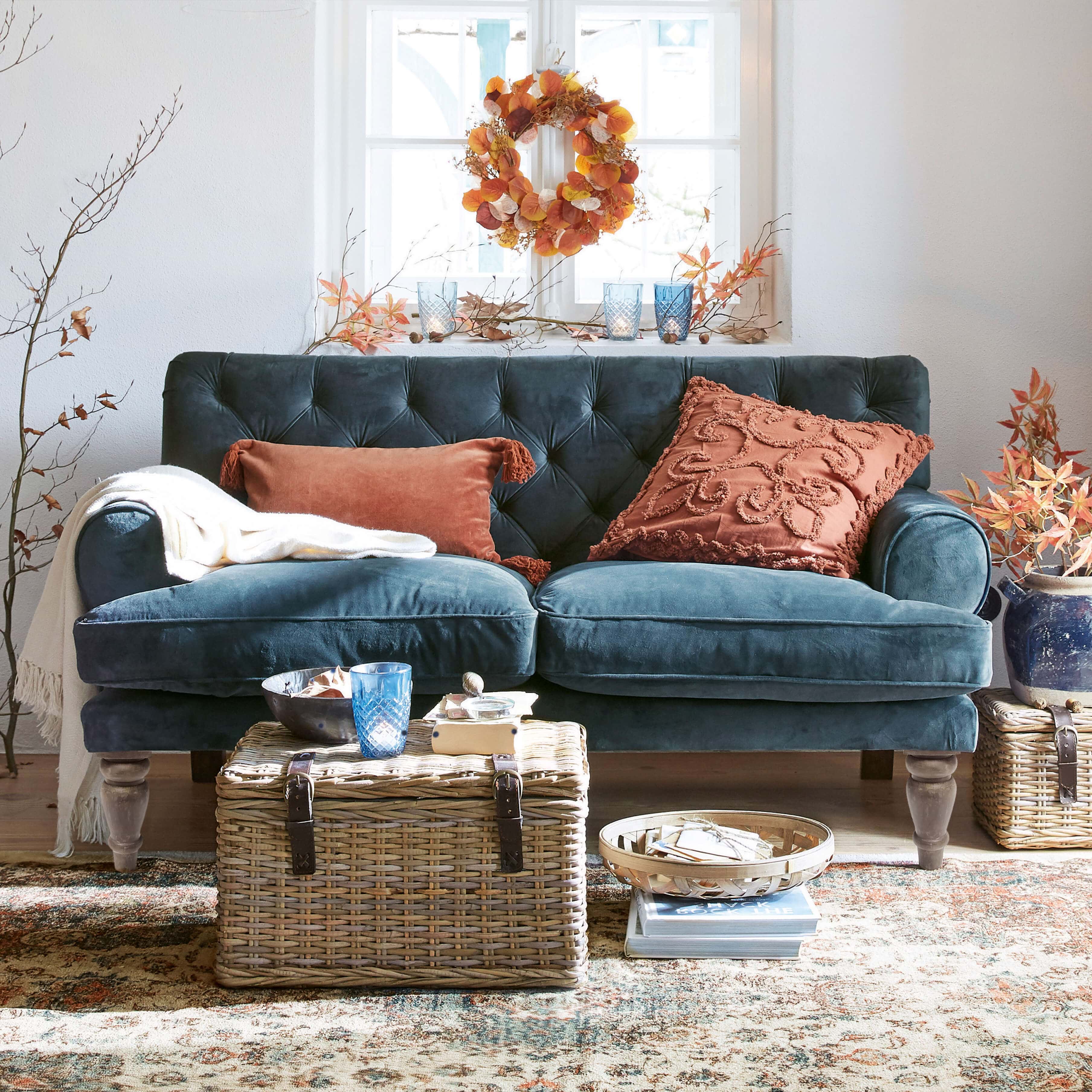 Canapé en velours bleu foncé avec coussins rouille et table en osier dans un salon chaleureux