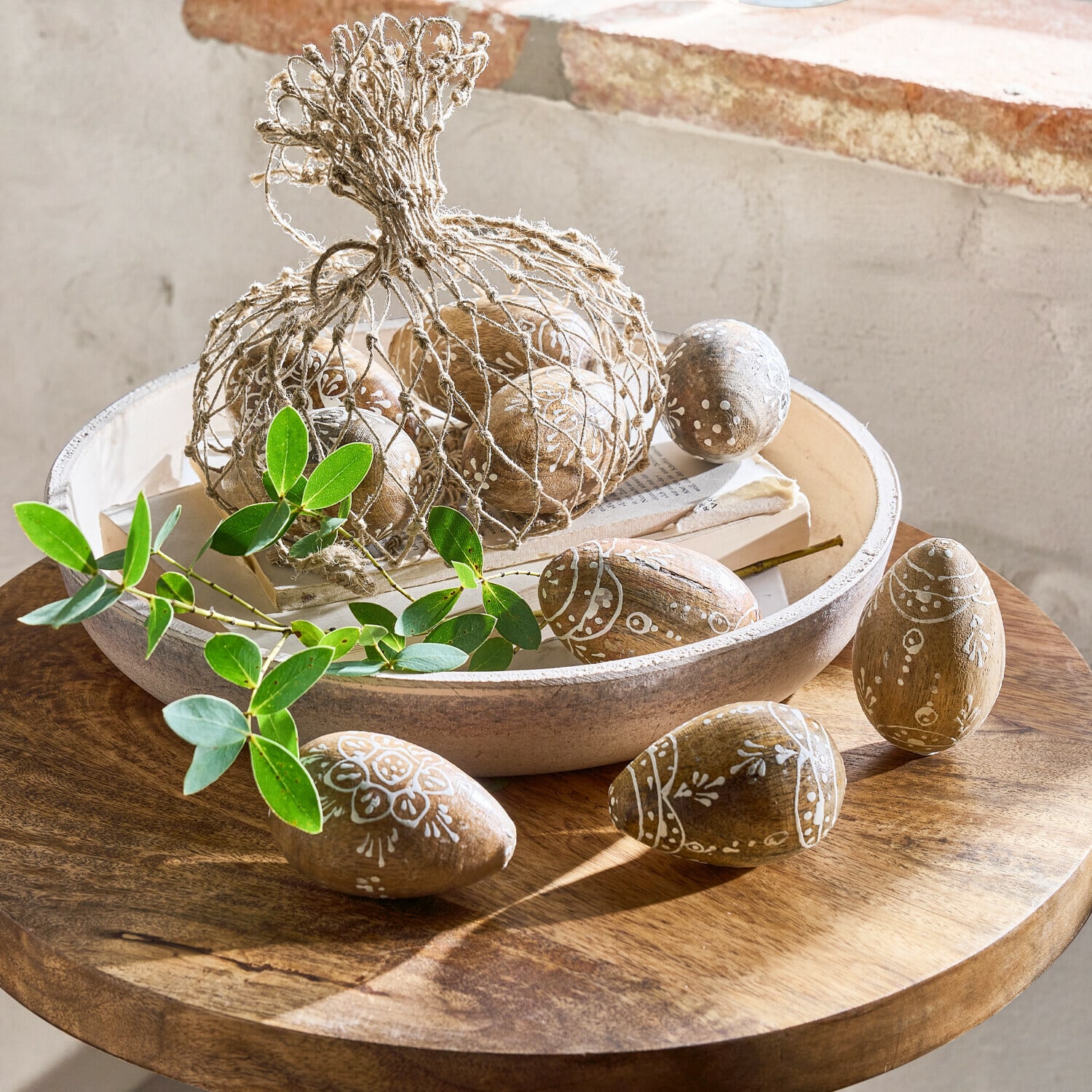 Lot de 9 œufs de Pâques Raylan Œufs en bois décorés de motifs blancs dans un bol sur une table en bois avec des feuilles vertes