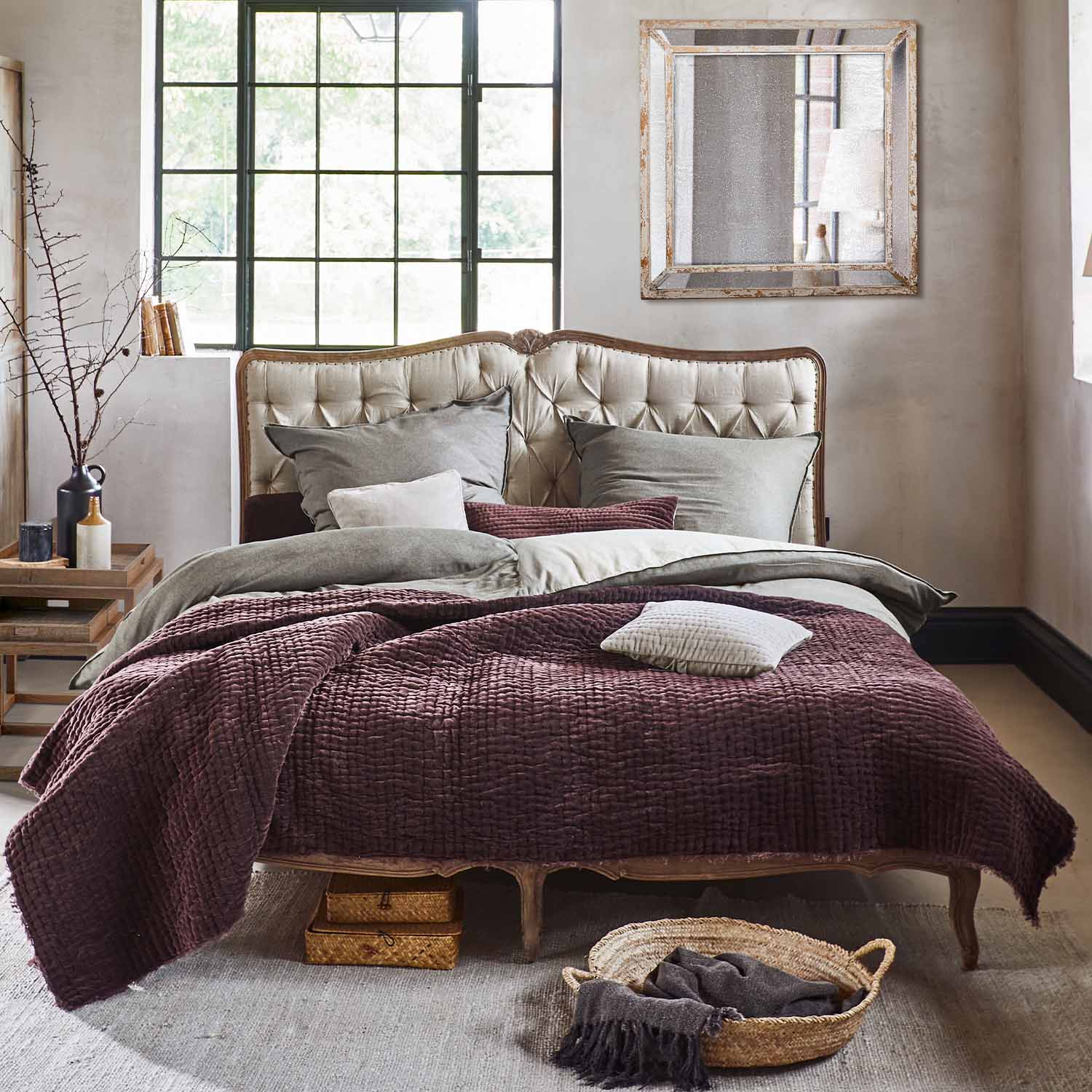 Lit avec tête de lit capitonnée beige et couverture bordeaux en tissu doux dans un style vintage