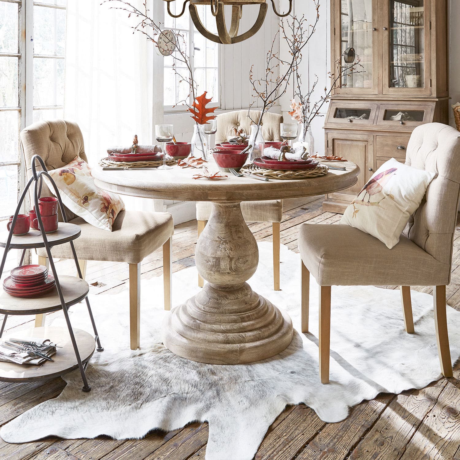 Table Orlin Table ronde en bois clair avec chaises rembourrées beige et vaisselle rouge dans une salle à manger lumineuse