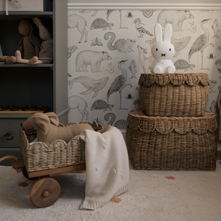 Deux paniers en osier marron avec une lampe lapin et des jouets dans une chambre d'enfant avec papier peint animalier