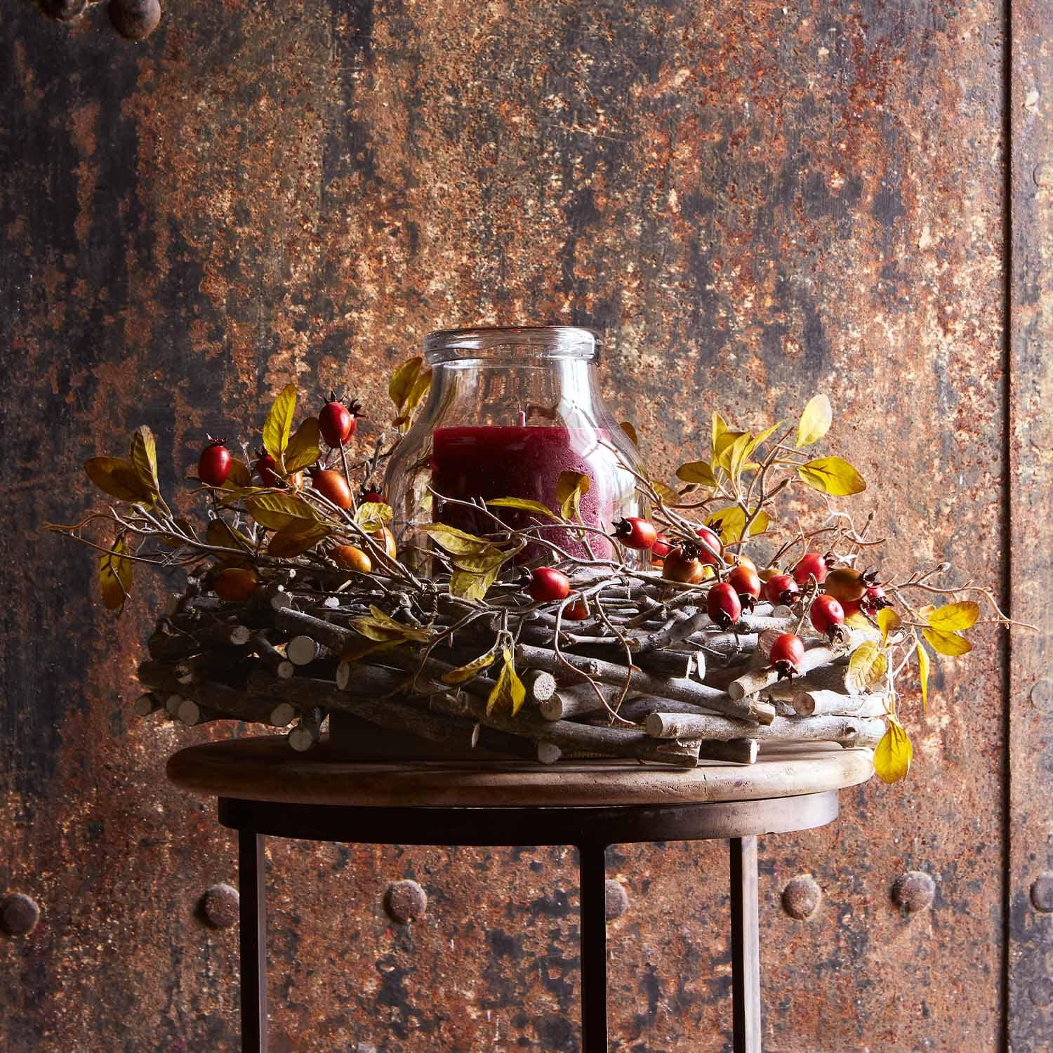 Couronne décorative en branches avec baies rouges et bougie rouge en verre sur table en bois