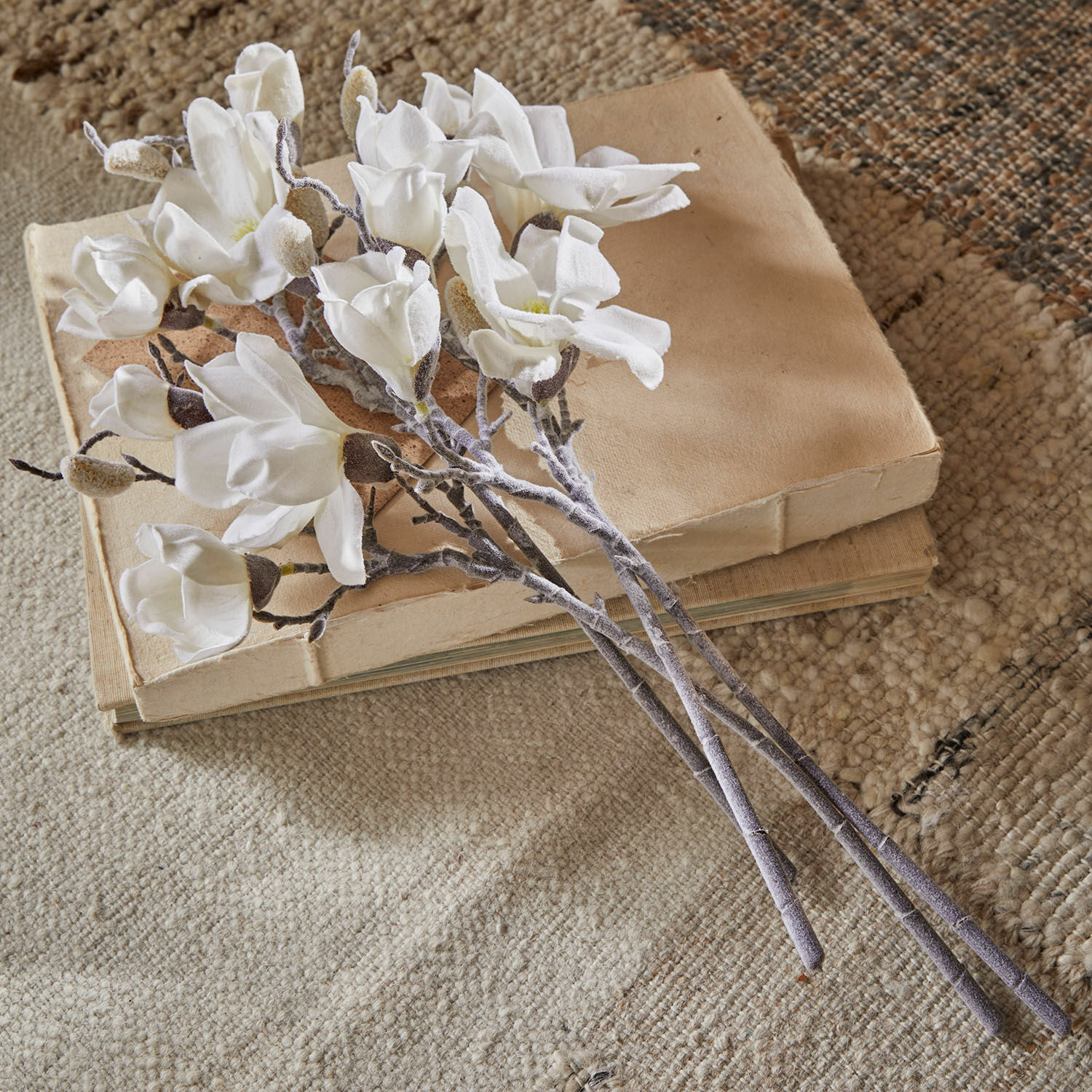 Lot de 4 fleurs décoratives Santavella Bouquet de fleurs de magnolia blanches en tissu posé sur des livres beiges sur un tapis texturé