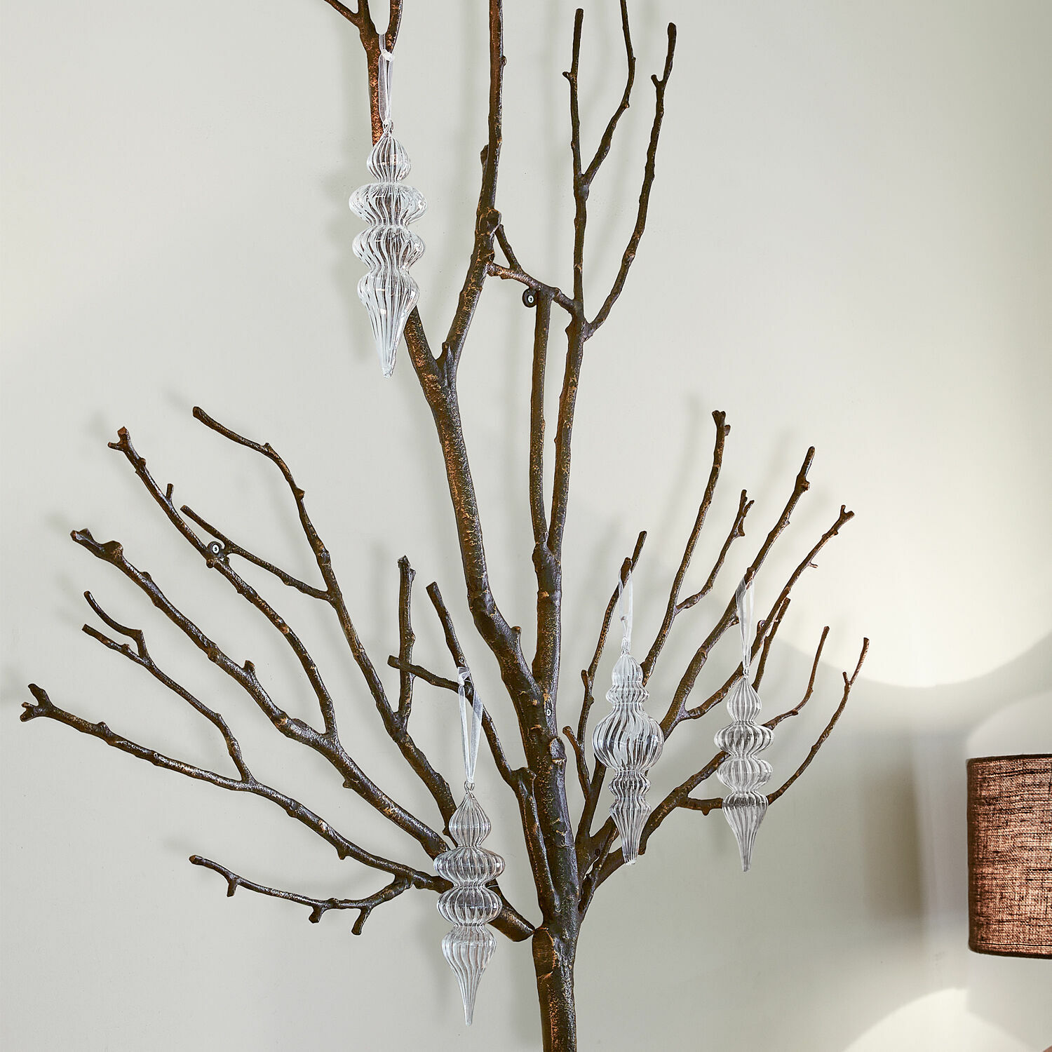 Lot de 4 décorations de Noël Diorise Décorations transparentes suspendues sur des branches sombres contre un mur clair, décoration intérieure