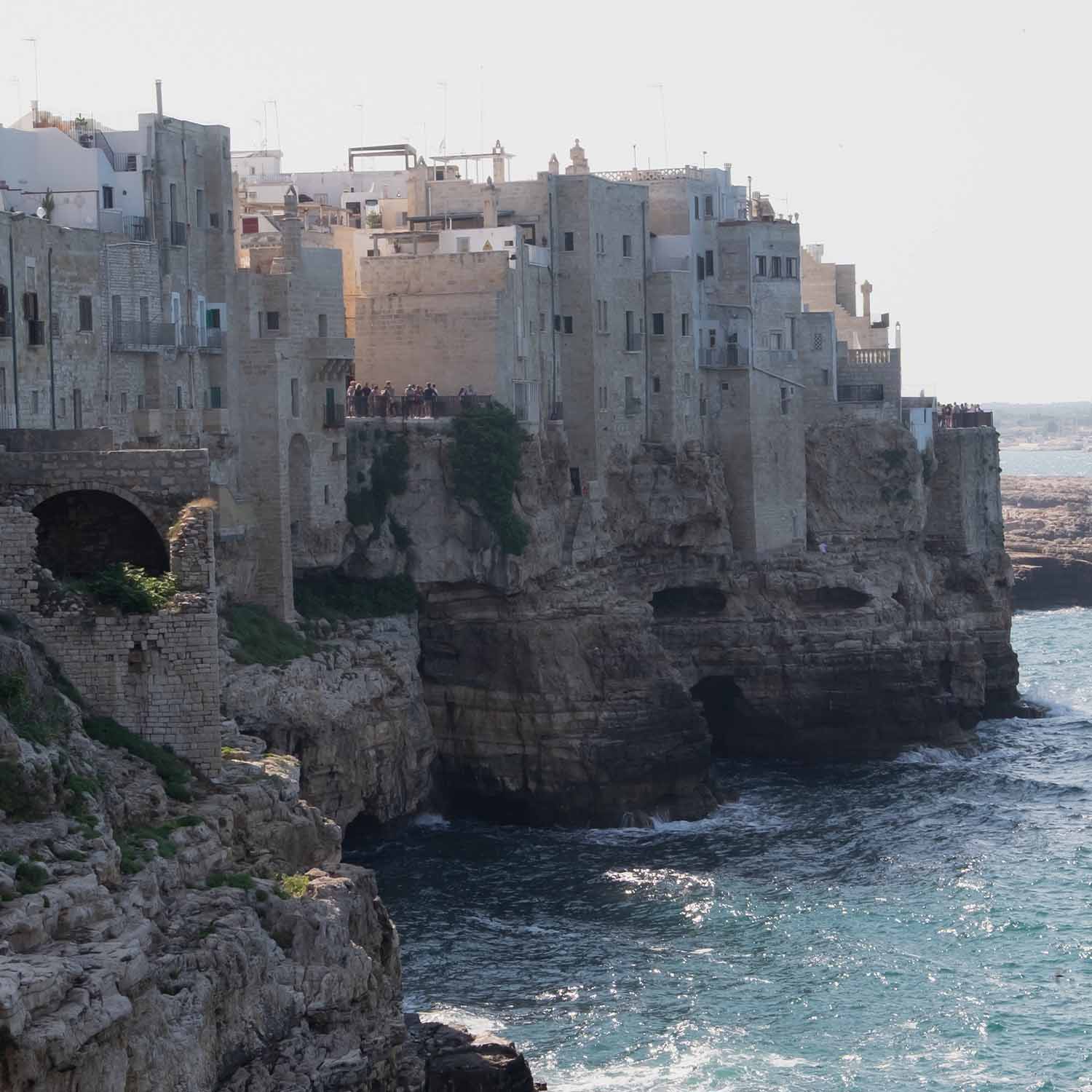 Anciennes maisons en pierre sur une falaise au bord de la mer avec des touristes et vagues