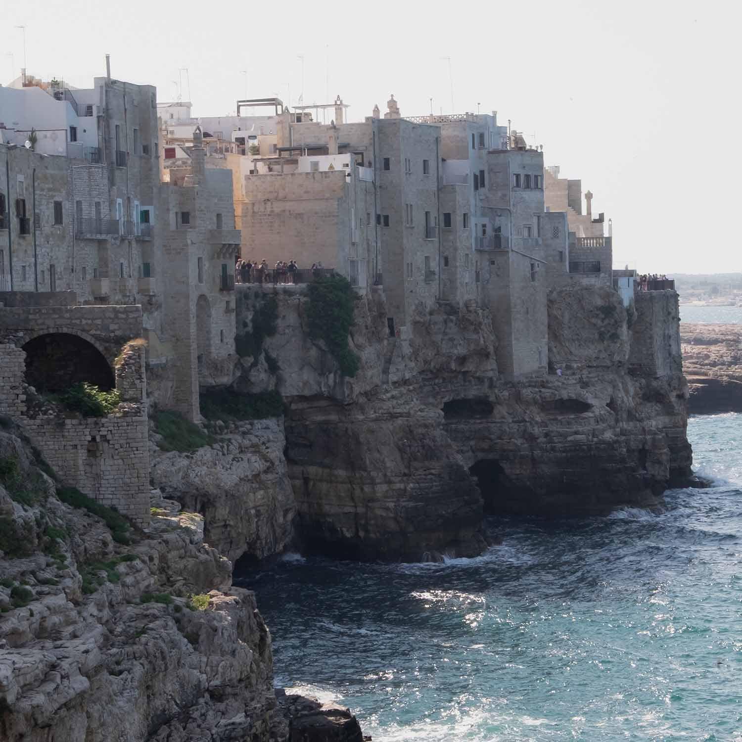 Anciennes maisons en pierre sur une falaise au bord de la mer avec des touristes et vagues