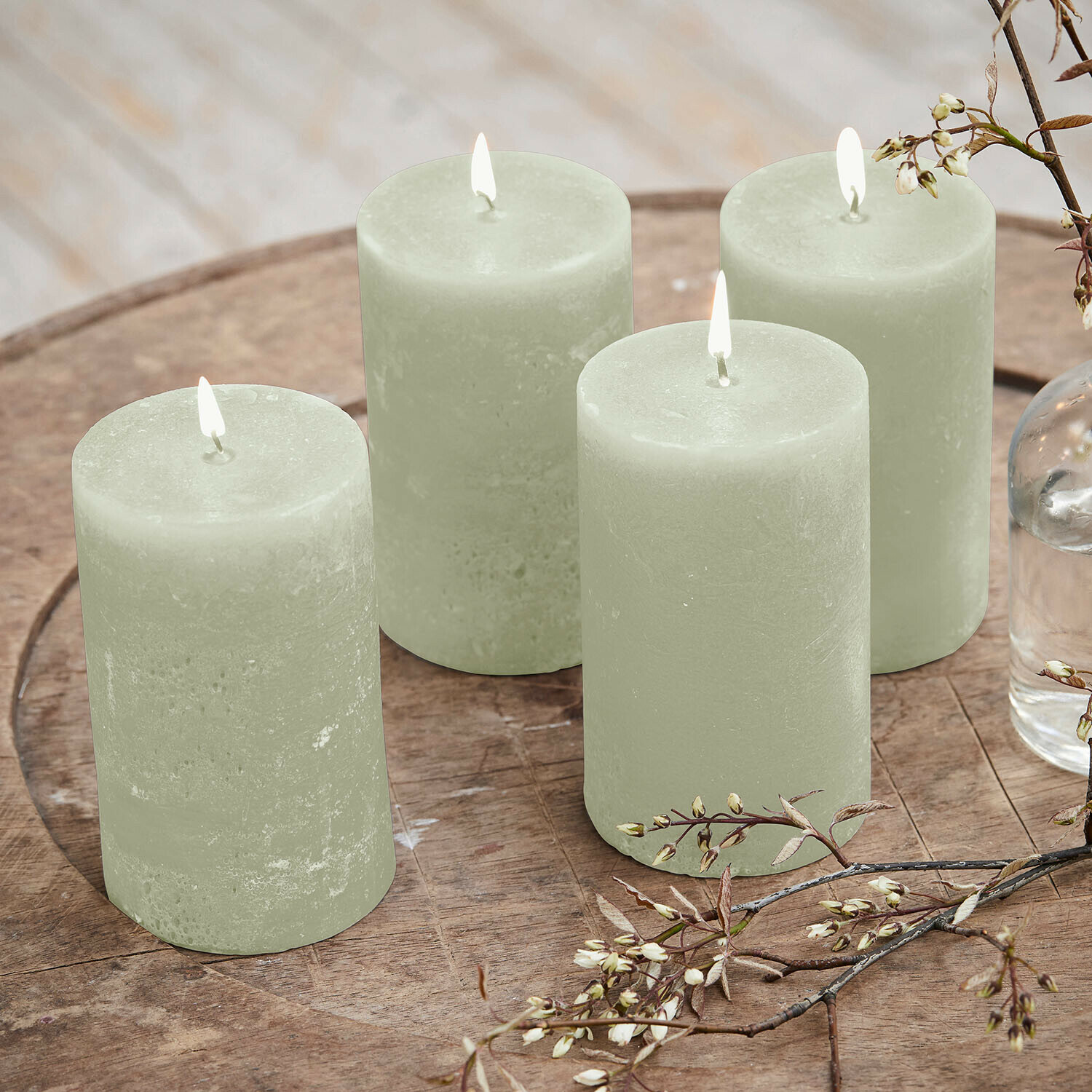 Lot de 4 bougies Braga Ensemble de quatre bougies vertes en cire sur une table en bois avec décoration florale