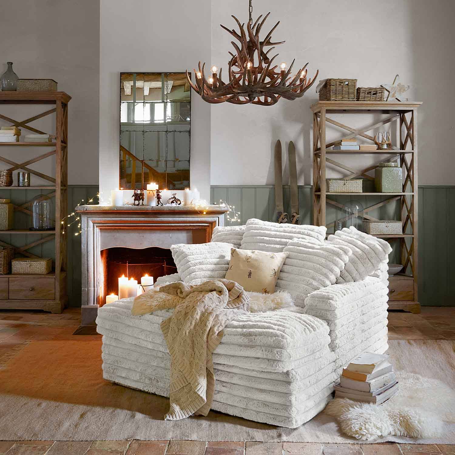 Fauteuil blanc en tissu doux dans un salon rustique avec cheminée et étagères en bois décoratives