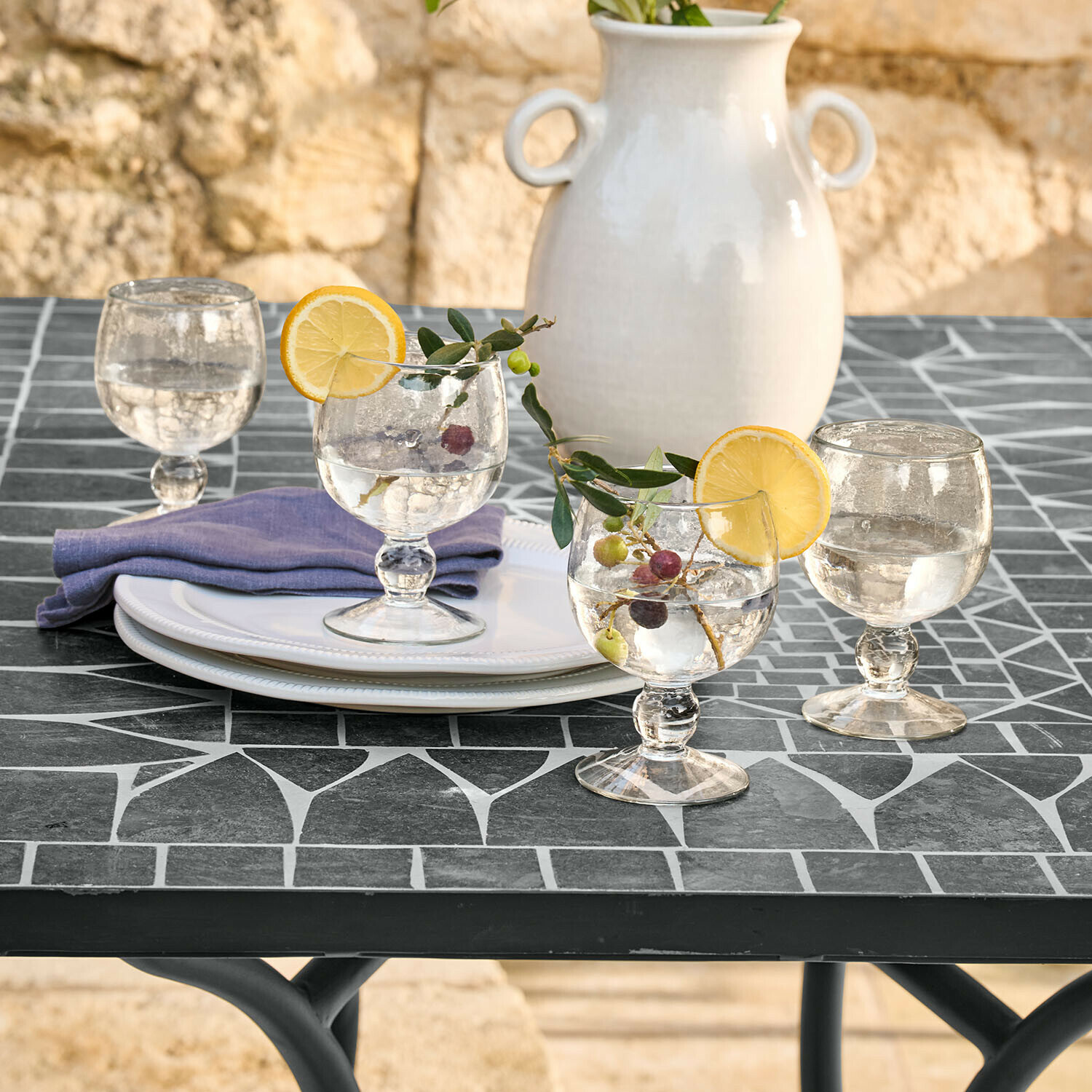 Lot de 4 verres Vinoros Verres en verre avec eau et tranches de citron sur table noire en mosaïque, vase en céramique blanche en arrière-plan