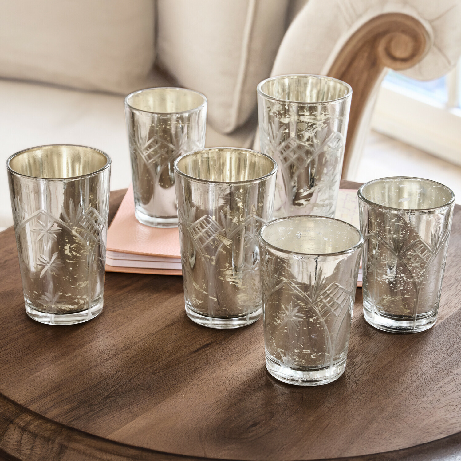 Ensemble de six photophores en verre gravé avec finition argentée posés sur une table en bois