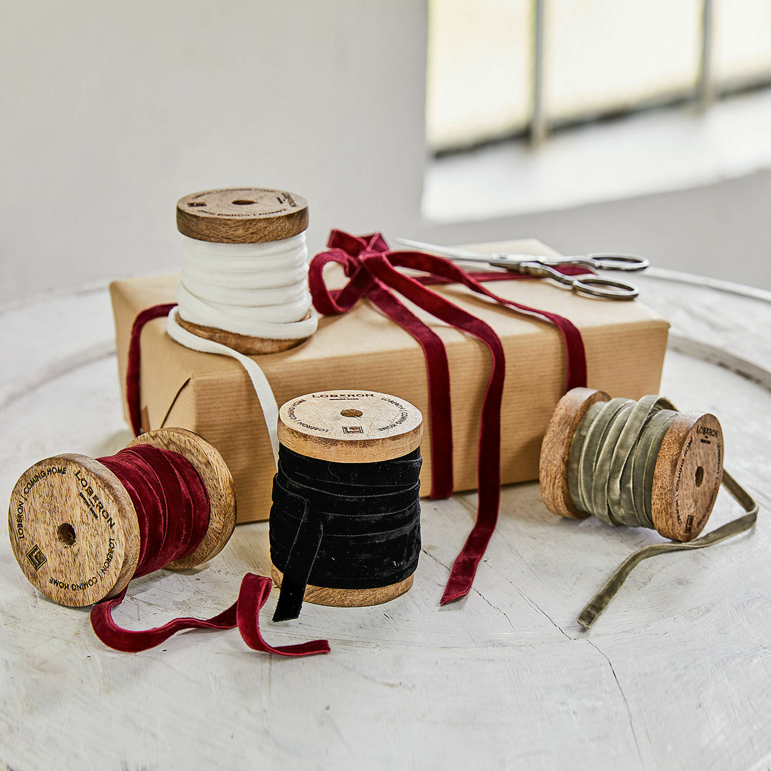 Lot de 4 rubans de velours Hilary Ensemble de bobines avec rubans en velours blanc, rouge, noir et olive sur une table avec un cadeau