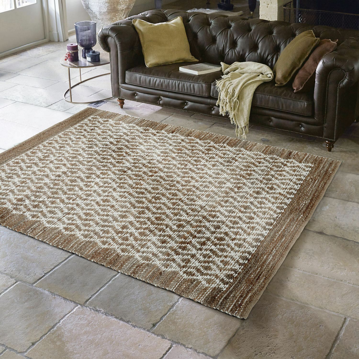 Tapis réversible Amhara Tapis marron et crème à motif géométrique sur sol en pierre devant un canapé en cuir foncé dans un salon