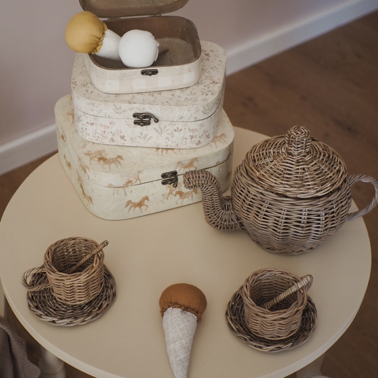 Service à thé pour enfants en osier avec théière et tasses sur une table ronde beige
