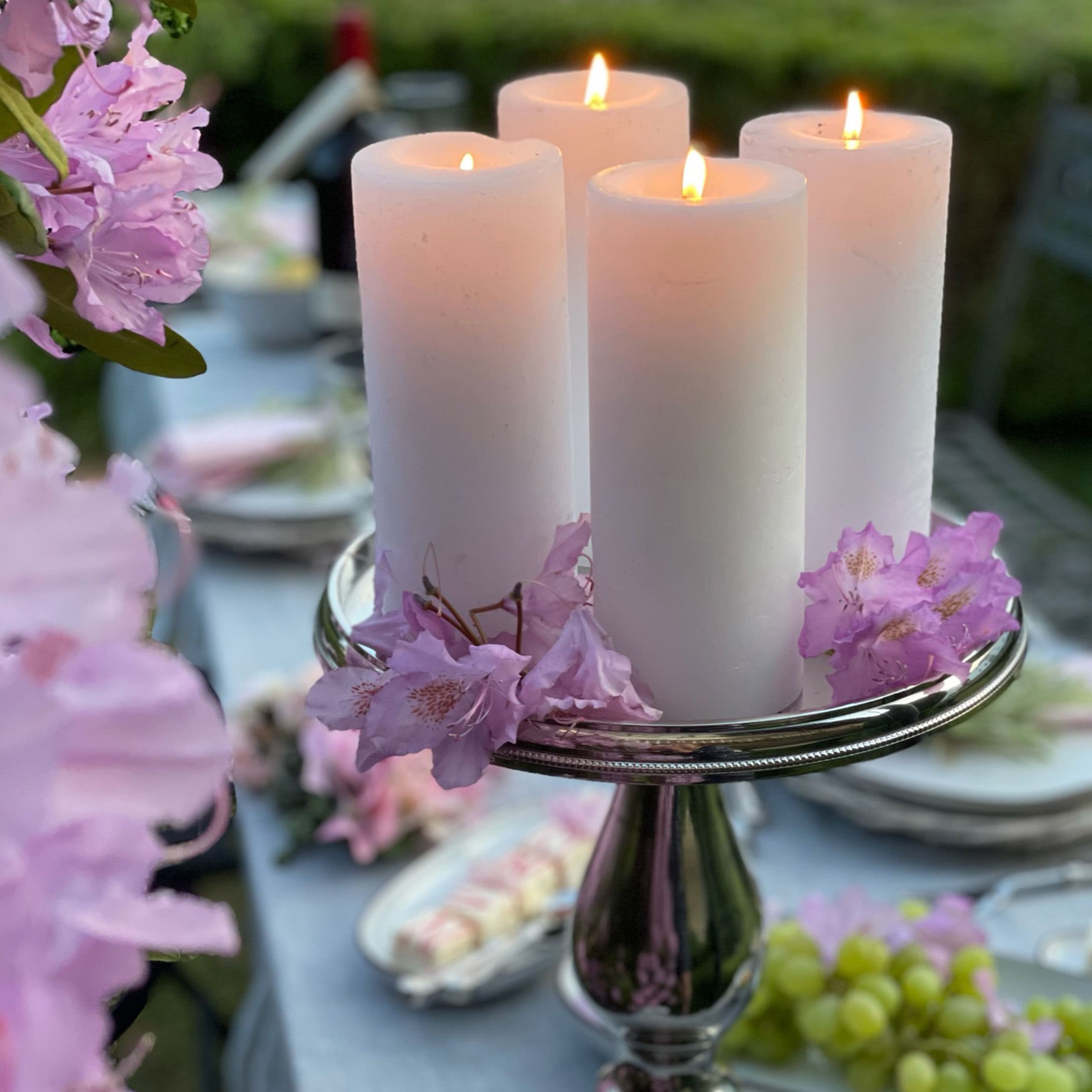 Quatre bougies blanches sur un chandelier argenté décoré de fleurs roses sur une table de jardin