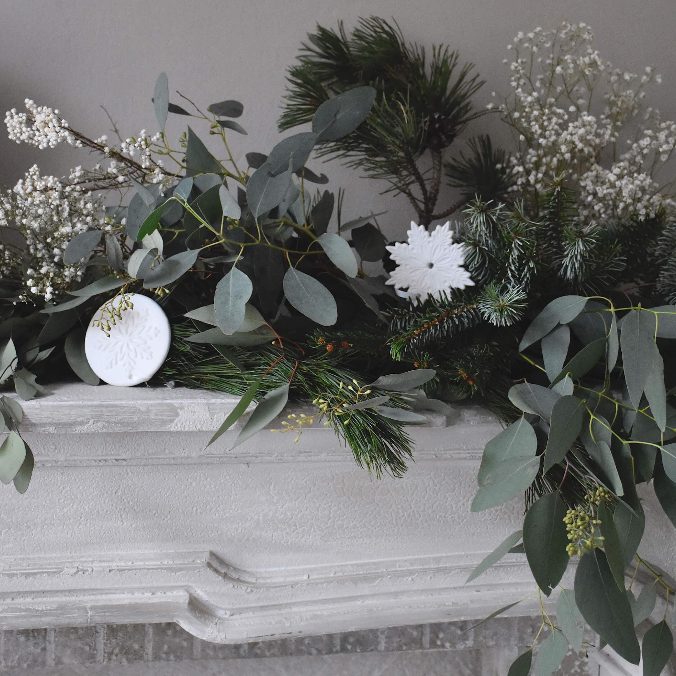 Couronne décorative en branches vertes et ornements blancs en forme de flocons sur une cheminée en pierre blanche