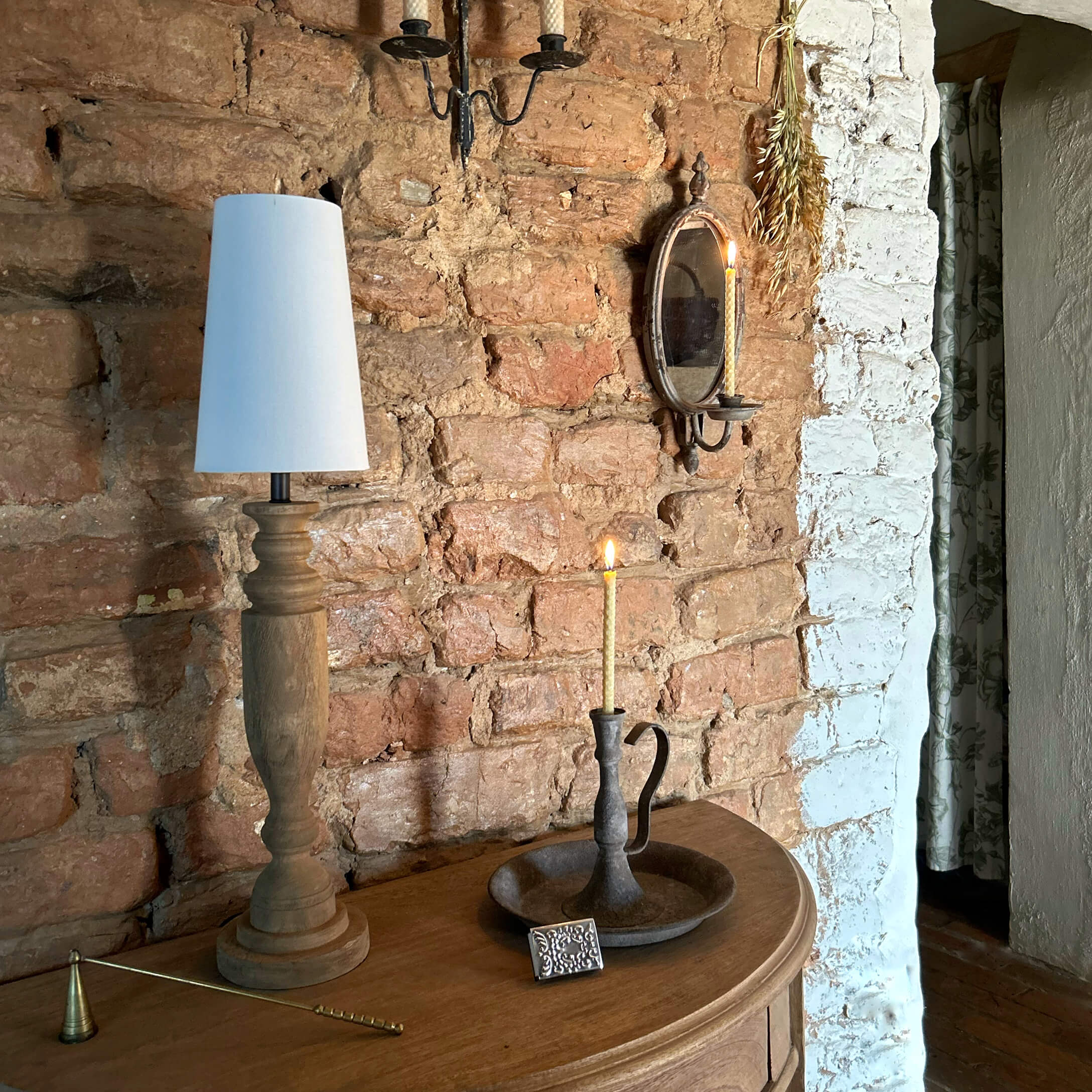 Lampe en bois avec abat-jour blanc et bougeoir en métal avec bougie allumée sur table en bois devant mur en briques