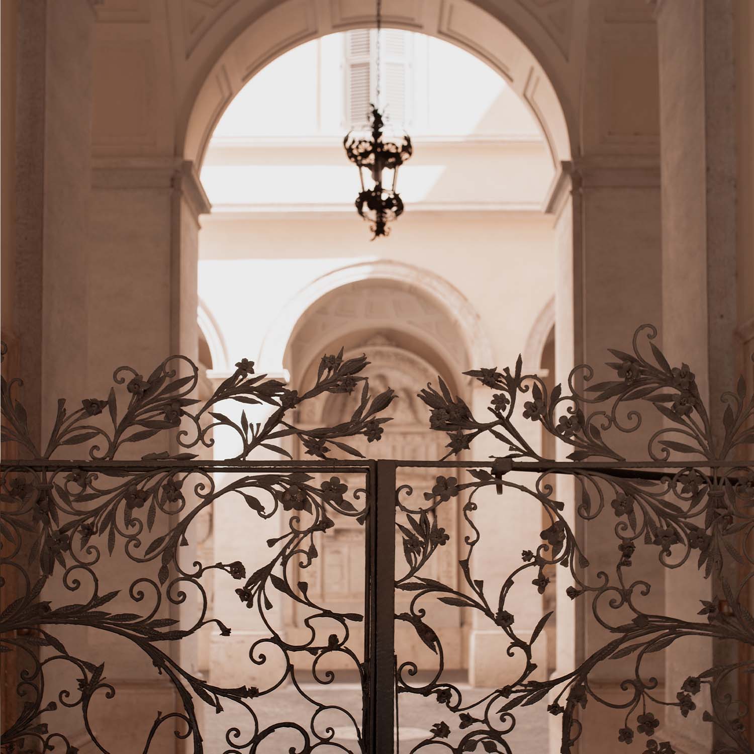 Portail en fer forgé orné de motifs floraux devant un intérieur lumineux aux arches claires